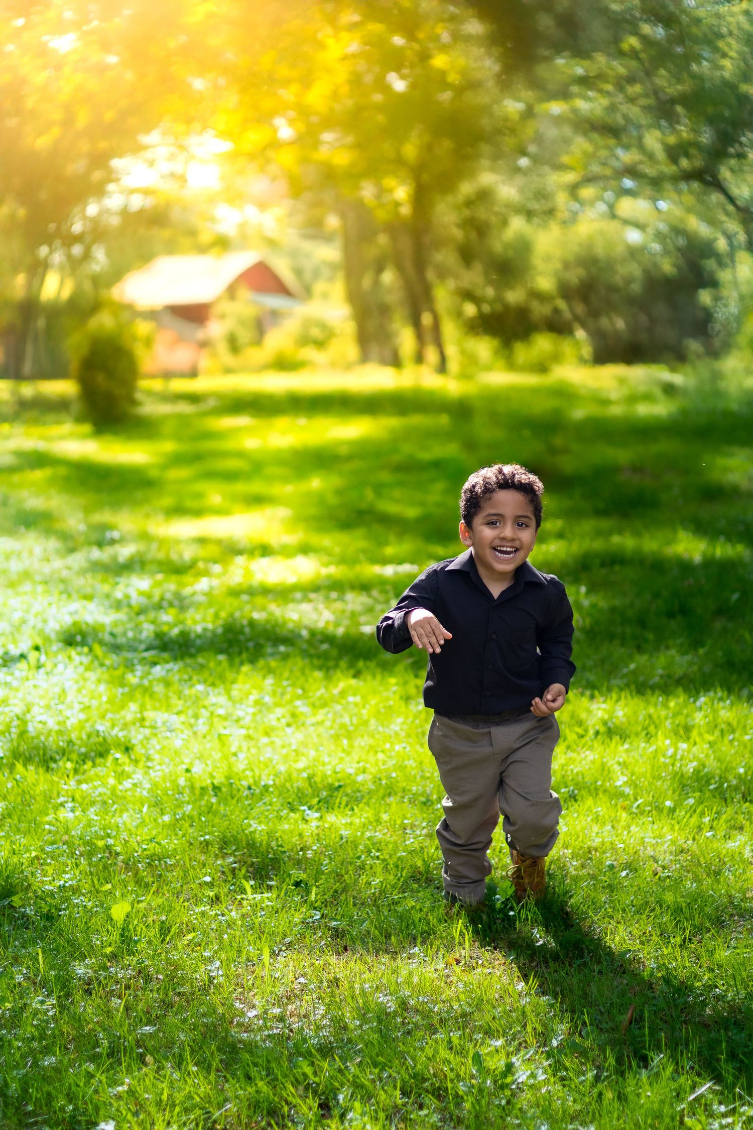 A young child runs playfully across a sunlit grassy lawn with a red barn visible in the background.