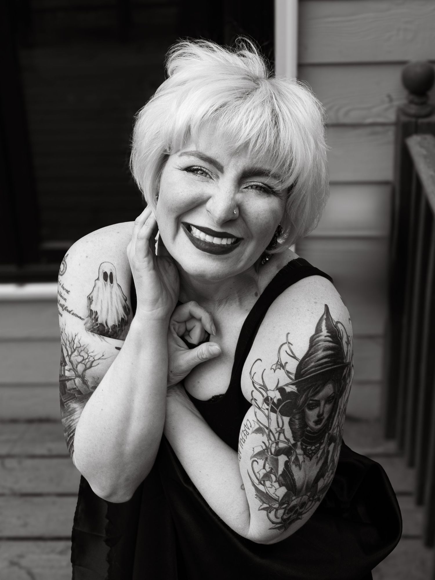 Smiling woman with short blonde hair and tattoos on both arms poses in black and white portrait photo.