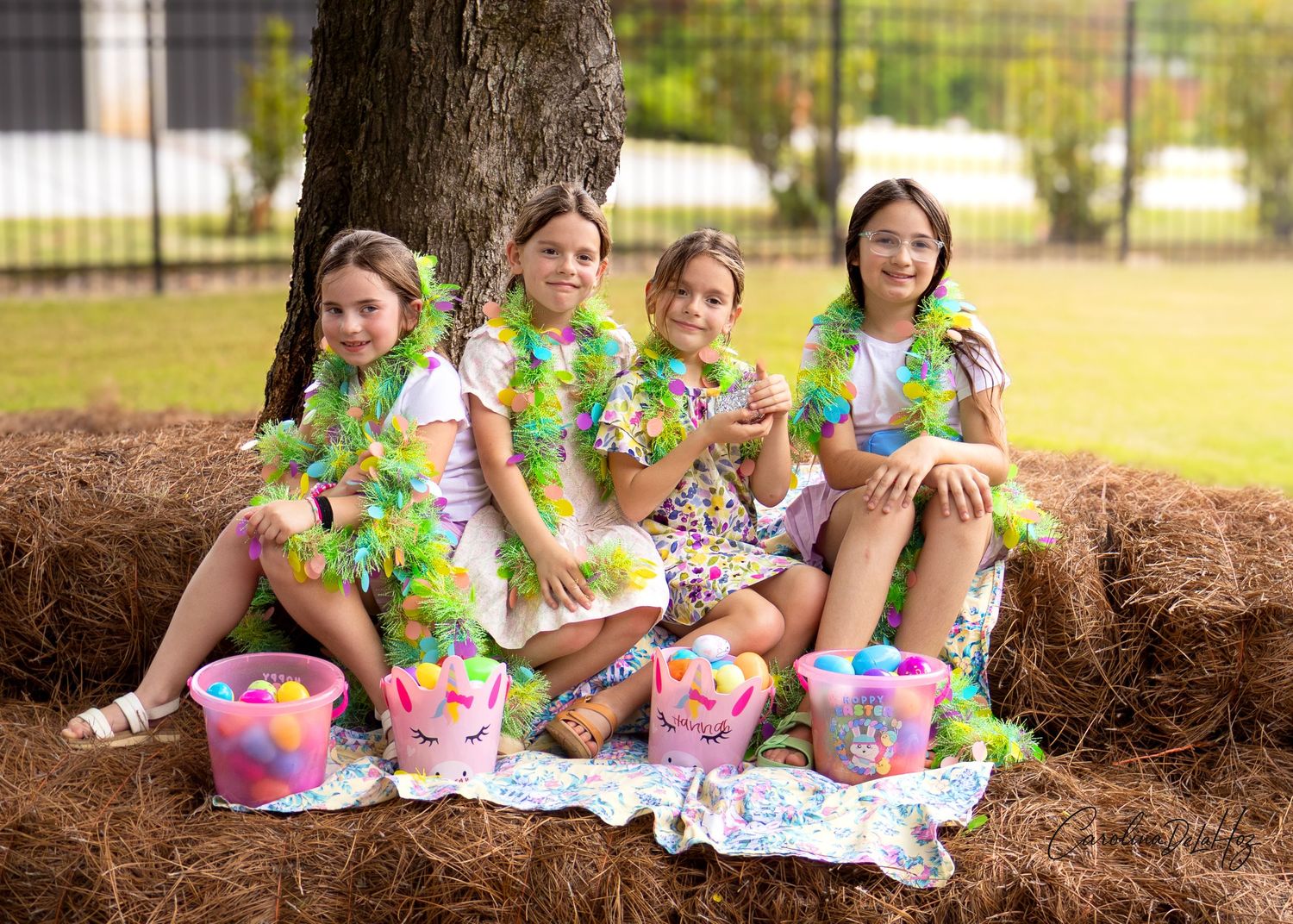 A group wearing floral print outfits sits on hay bales for an outdoor spring-themed photoshoot with colorful baskets.