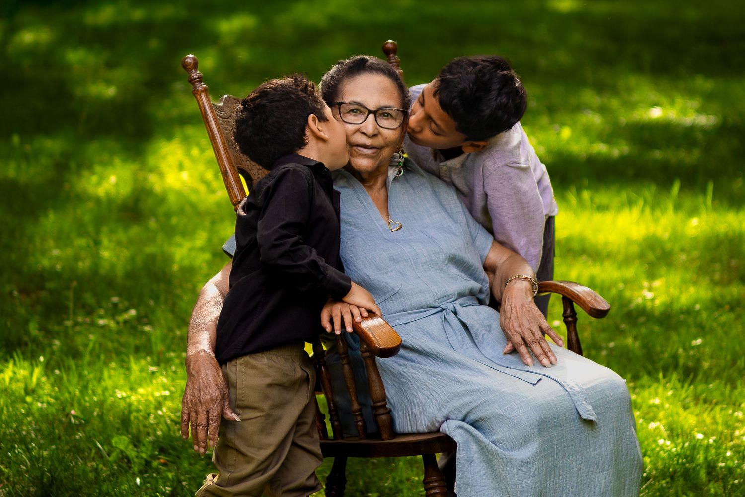 A person in a wheelchair sits in a sunny garden while being lovingly embraced by two children.
