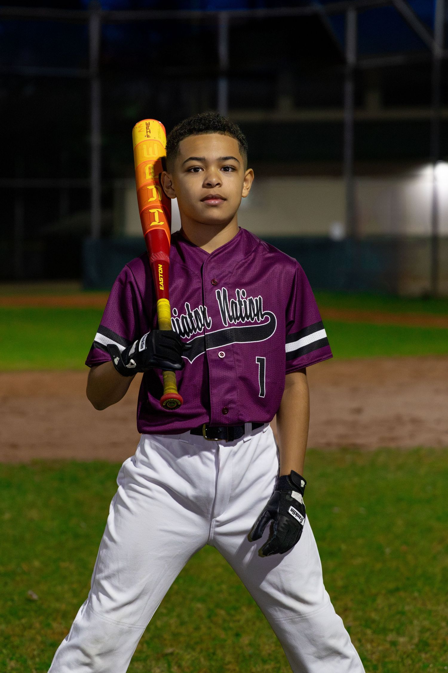Baseball player in purple jersey holding yellow bat on baseball field at night.