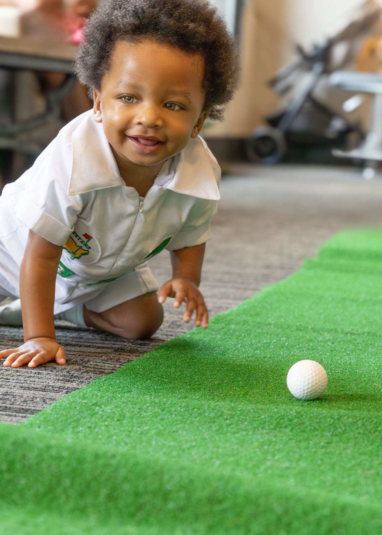 Small child crawling on green turf surface following a golf ball.