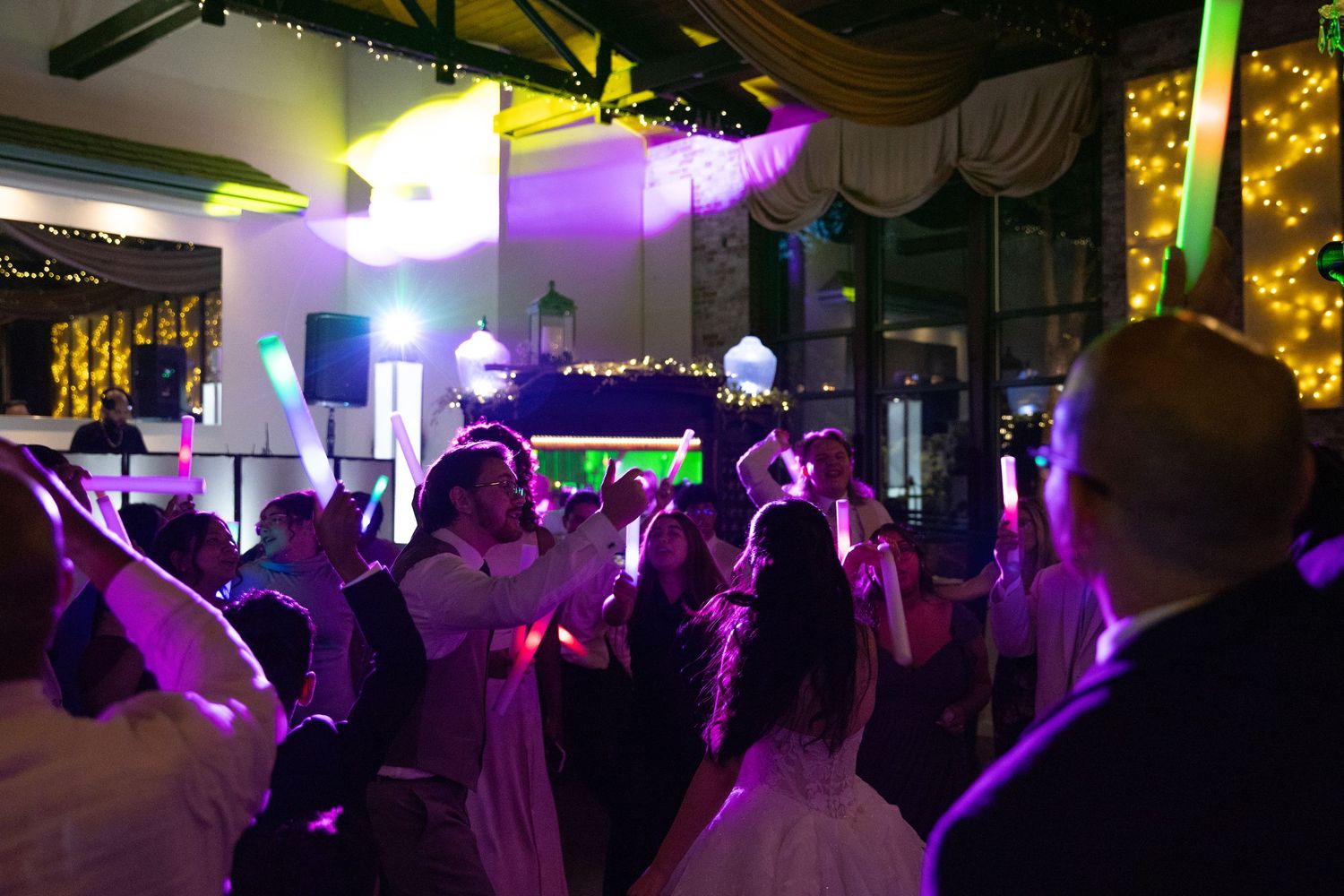 Guests dancing at a lively wedding reception with colorful purple and green lights illuminating the venue.