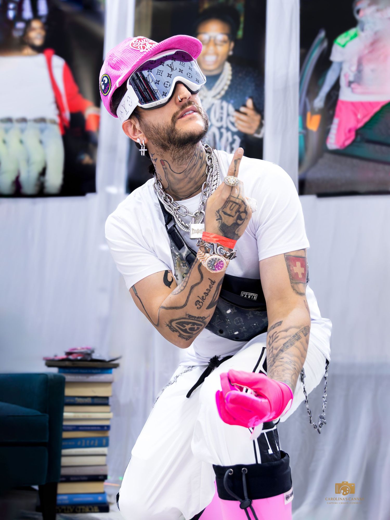 Tattooed man in white outfit with pink ski goggles and accessories posing outdoors at event.