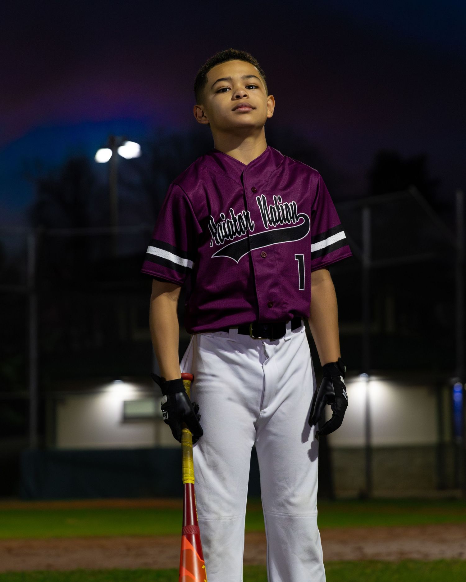Baseball player in purple jersey standing under stadium lights at night.