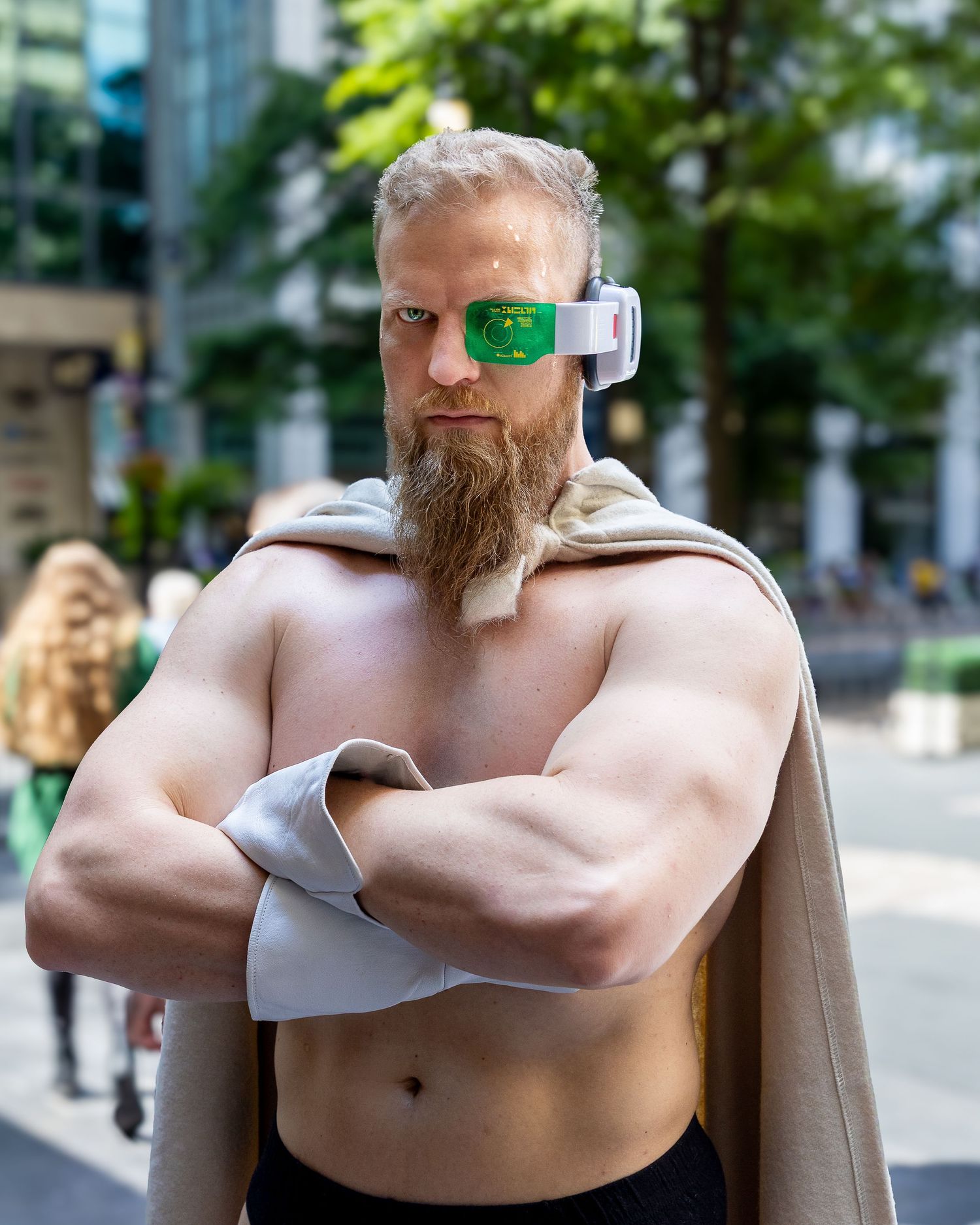 Muscular bearded man with cybernetic eye device poses shirtless against urban background in multiple views.
