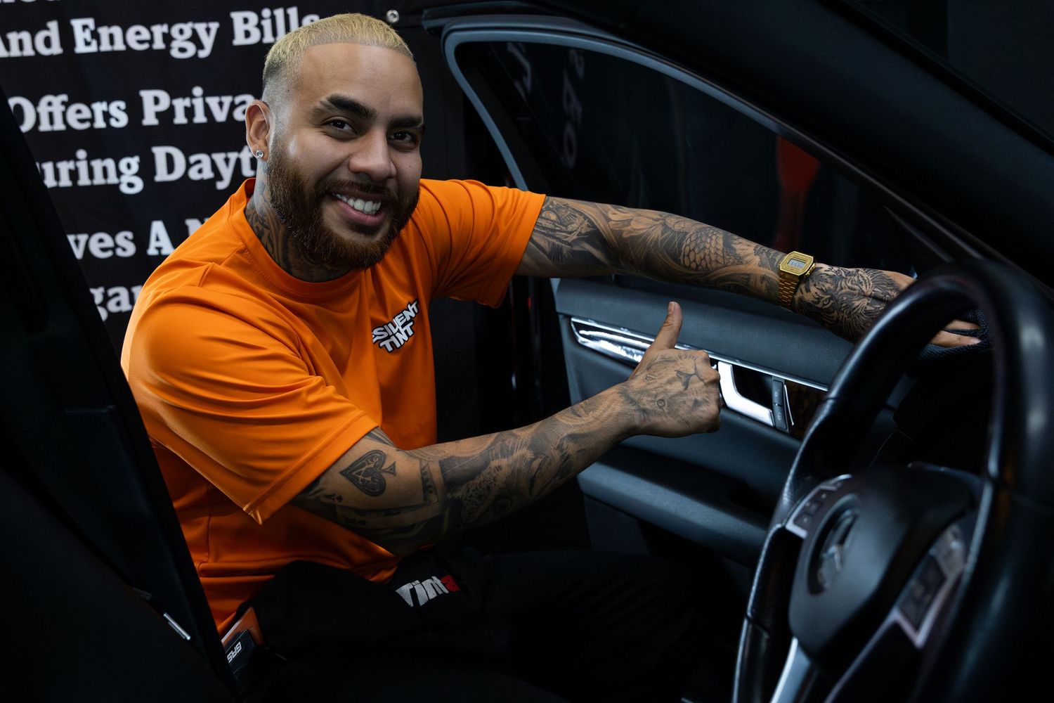 Someone wearing an orange t-shirt gives thumbs up while sitting in driver's seat of a car. marketing and business photography