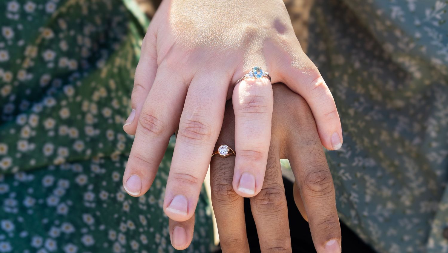 Close-up of two hands showing an engagement ring with a round diamond solitaire setting on a woman's finger.