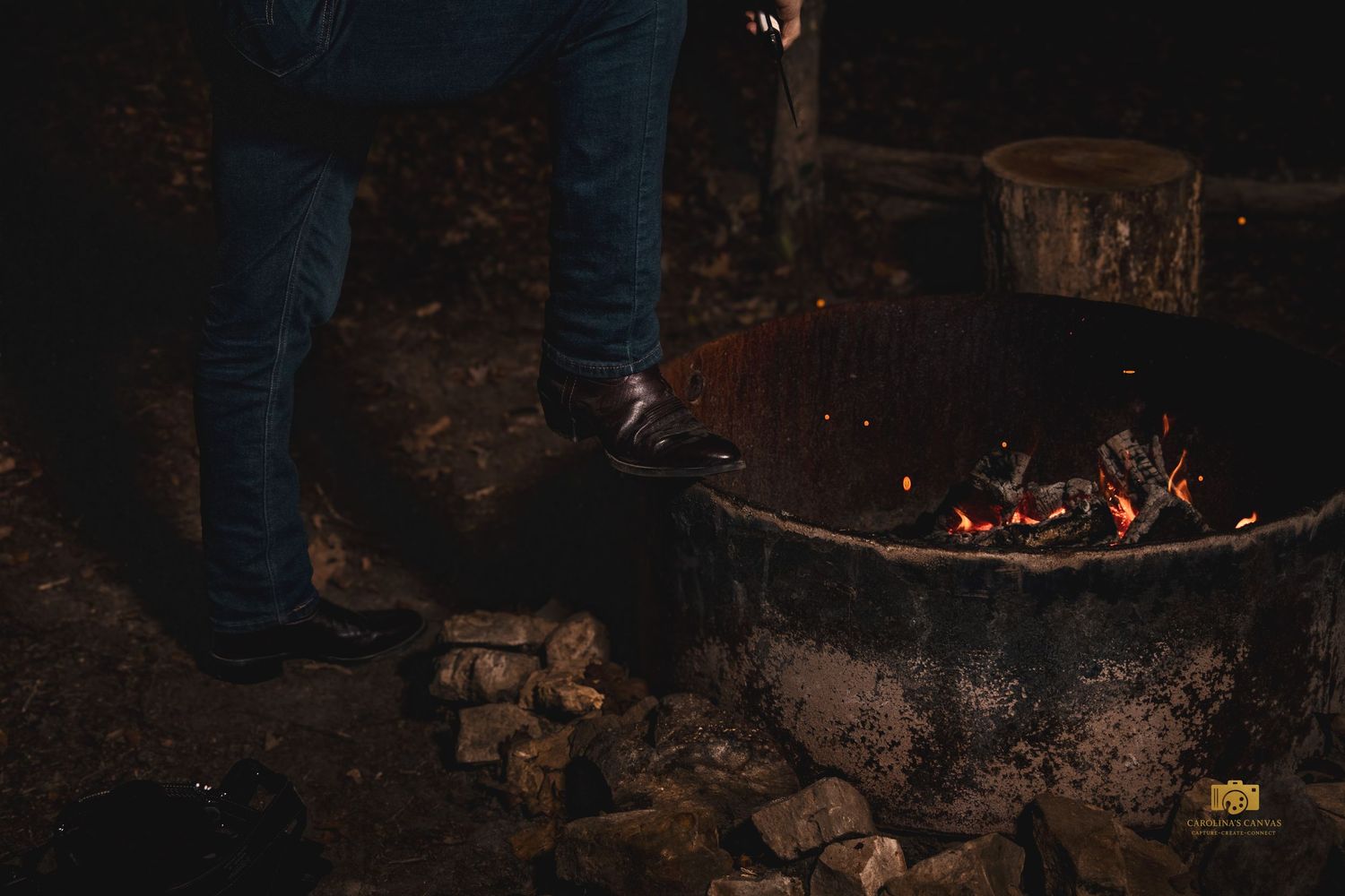 A row of glowing embers and burning logs in a dark fireplace or campfire setting.