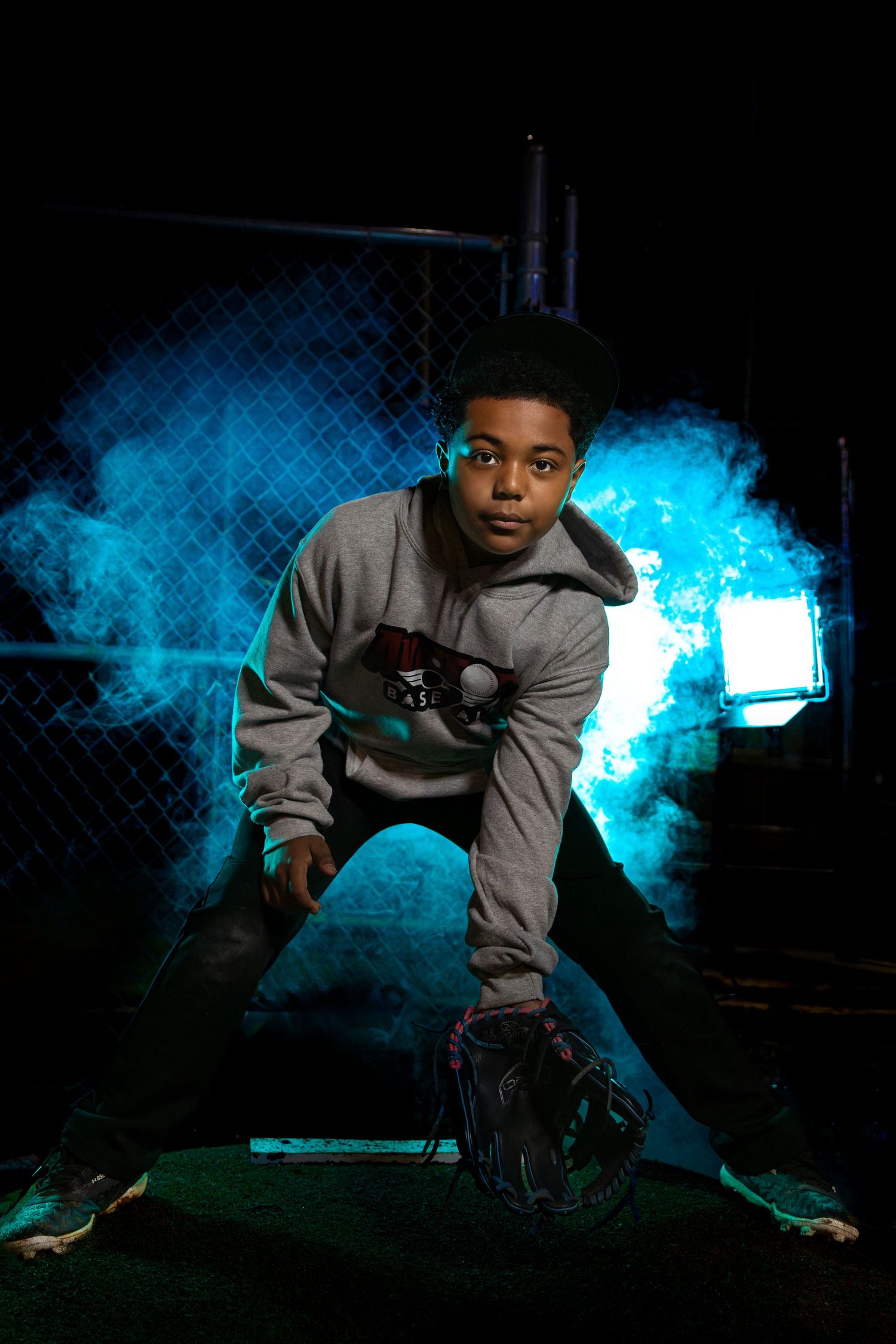 Athletic figure posing in grey hoodie against dramatic blue smoke and dark background.