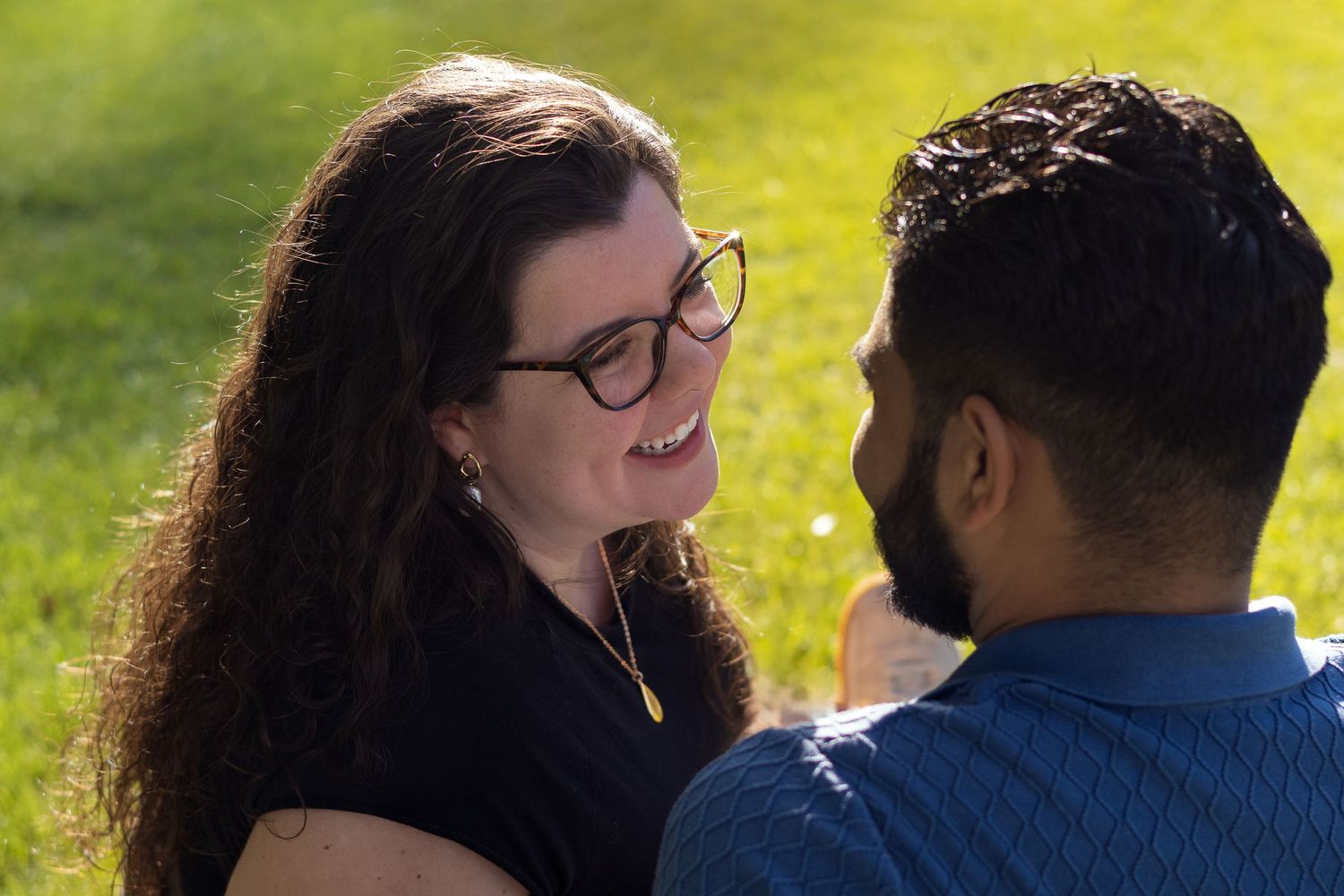 A couple sits together outdoors on a sunny day, sharing a warm moment against a bright green background.