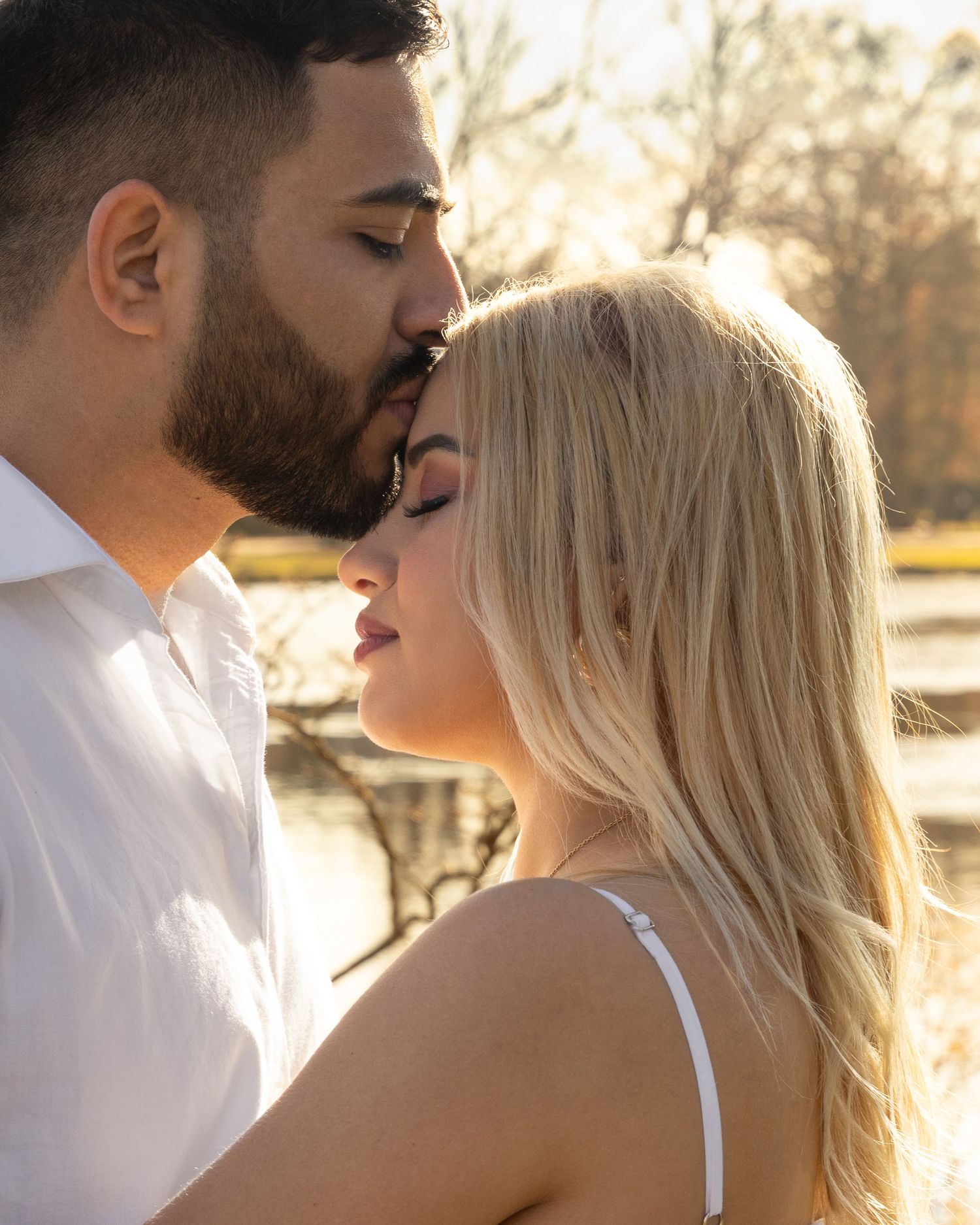 A couple shares an intimate moment in golden sunlight while standing close together outdoors.