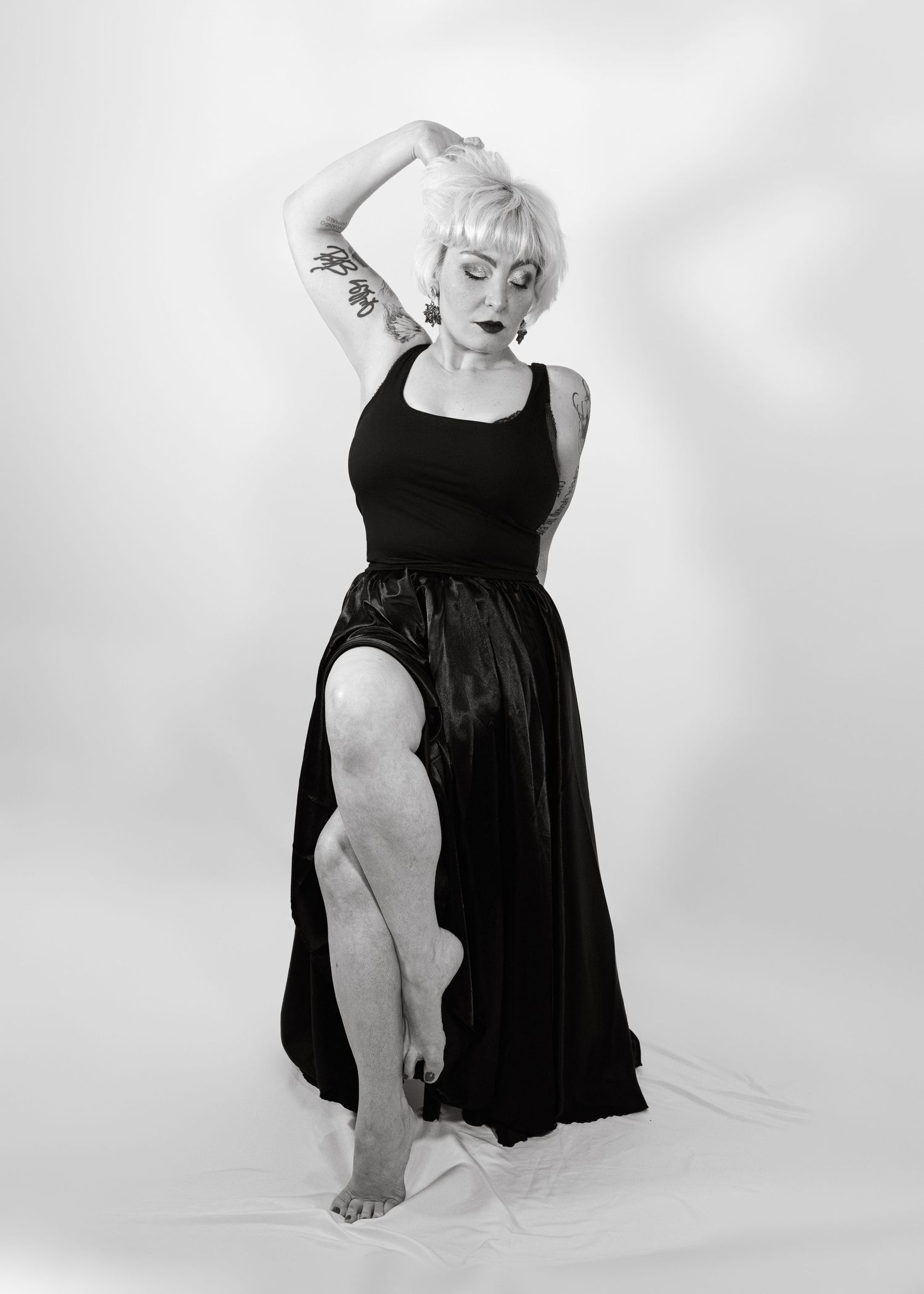 Black and white photo of a woman in a black dress posing gracefully with one arm raised and leg extended.