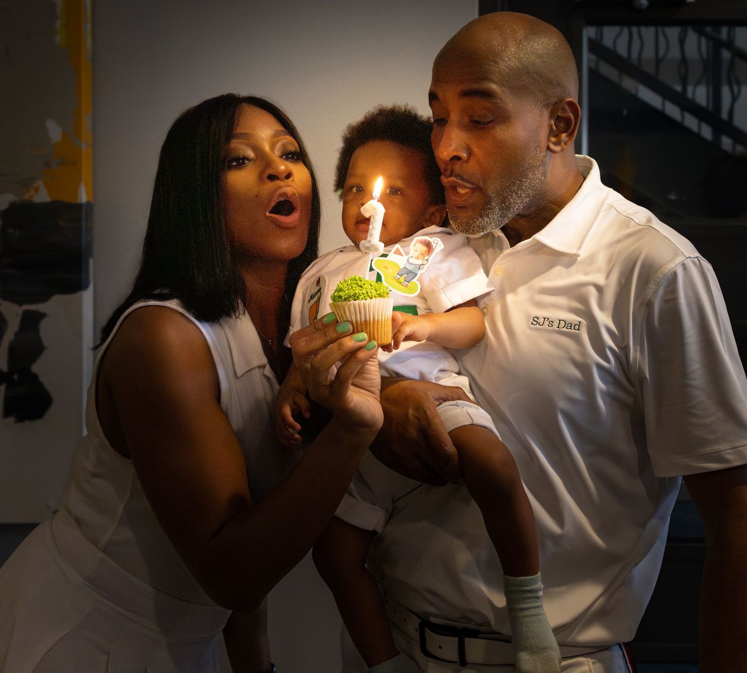 Two people blowing out a birthday candle together on a cupcake in a dimly lit setting.