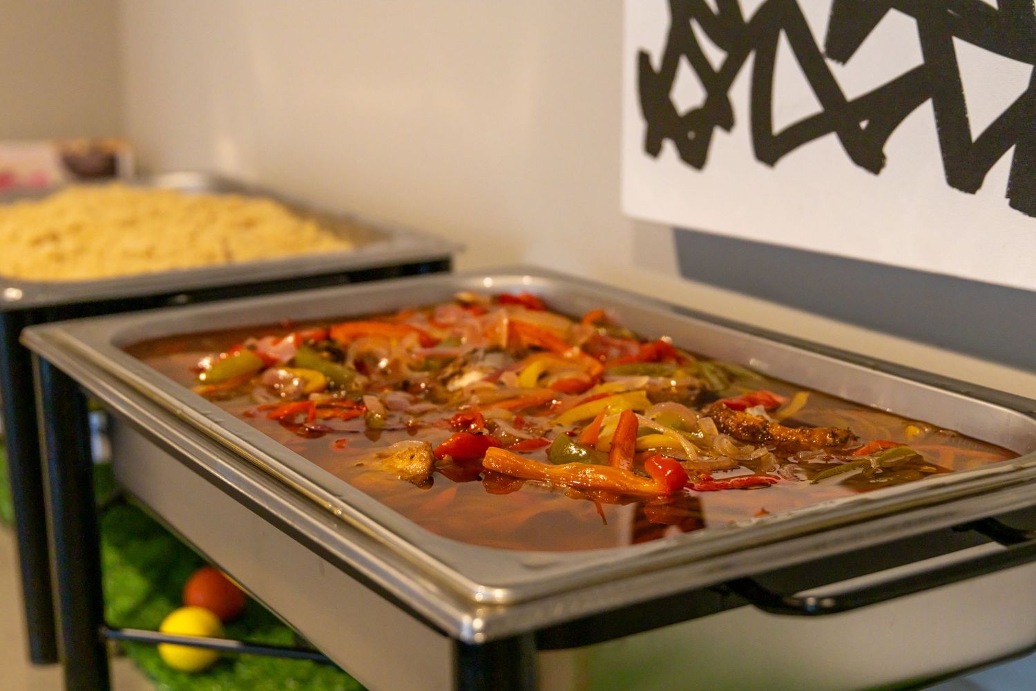 Metal trays filled with colorful roasted vegetables and meats on a commercial kitchen buffet line.