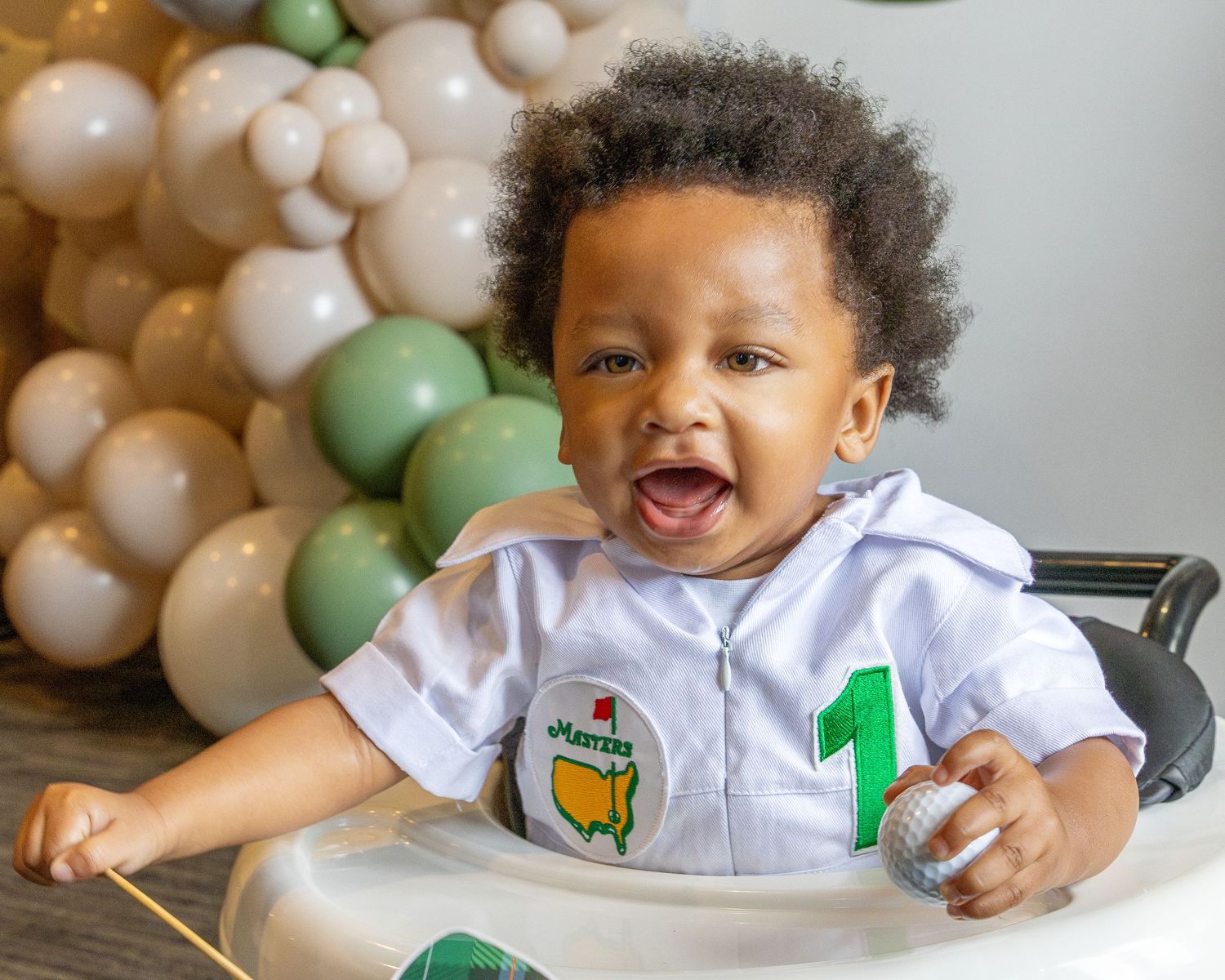 Festive first birthday celebration with green and white balloons and decorative party setup.