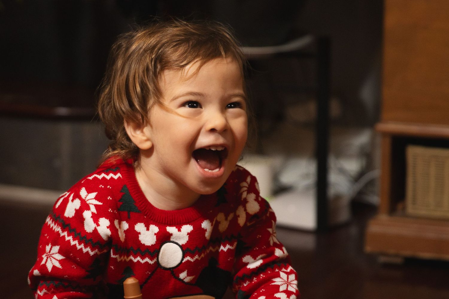 A joyful child wearing a festive red and white snowflake Christmas sweater laughs with pure delight.