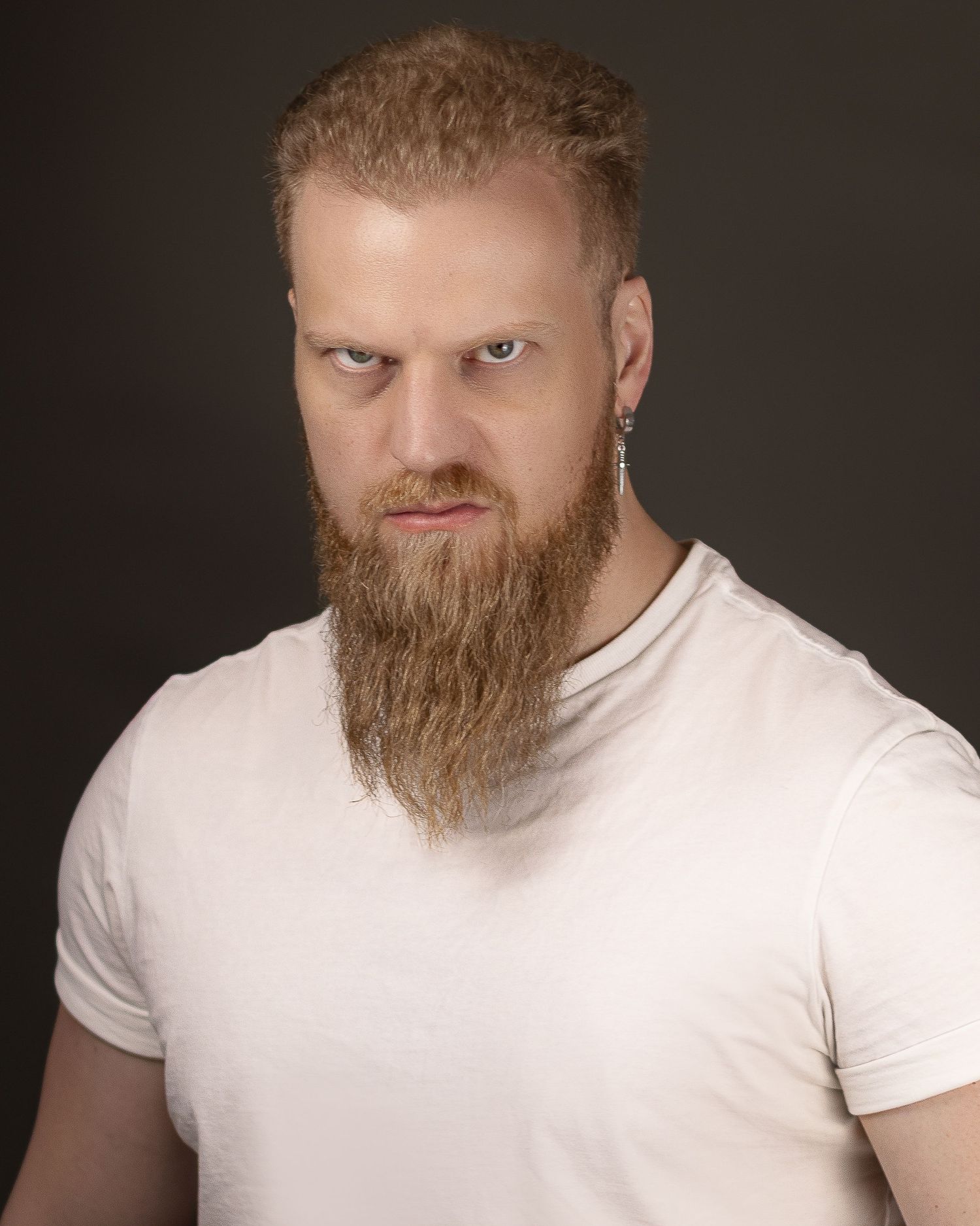 A person with a ginger beard in a white t-shirt poses against a dark studio background in a photo series.