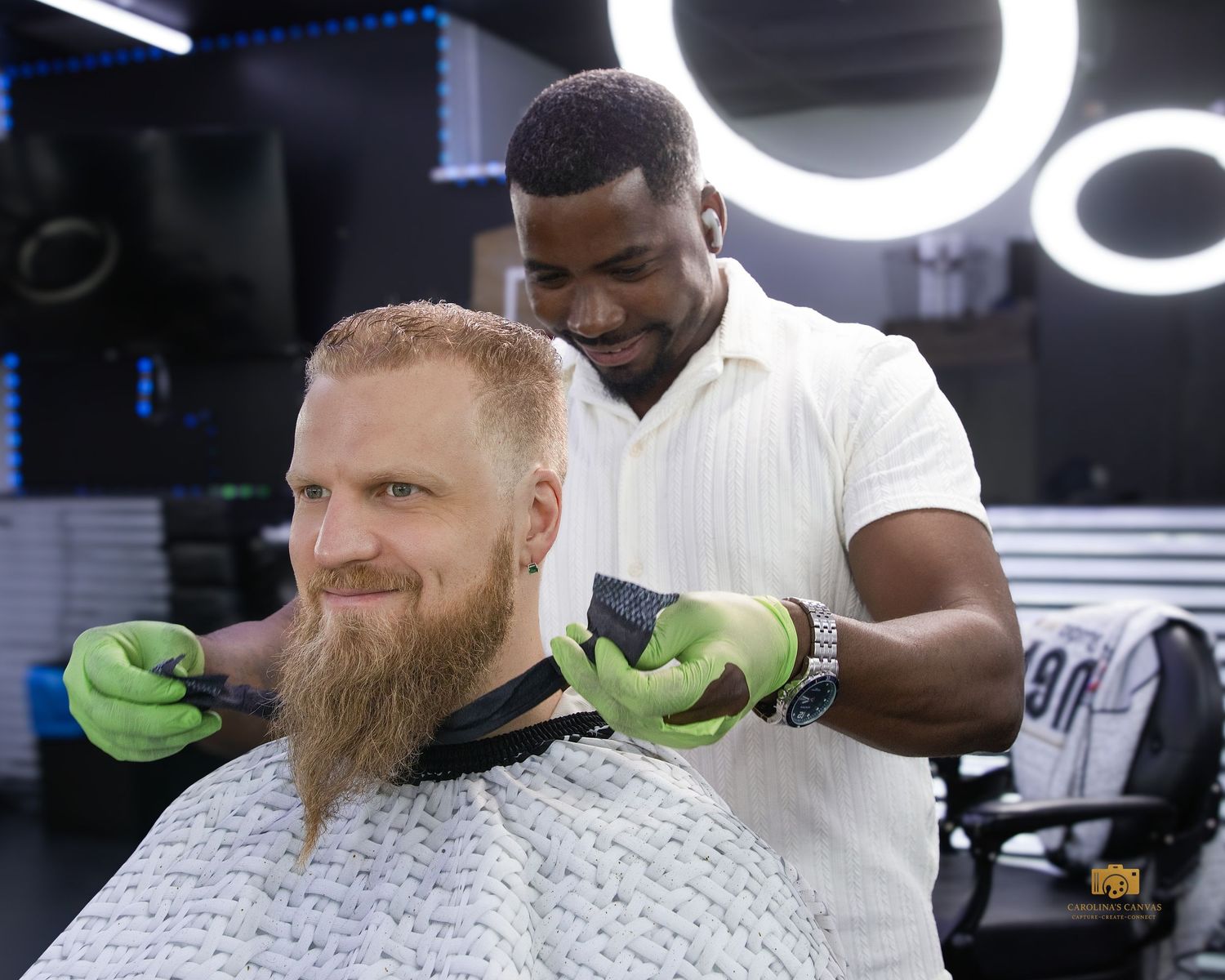 A barber wearing green gloves styles a client's hair in a modern barbershop setting.