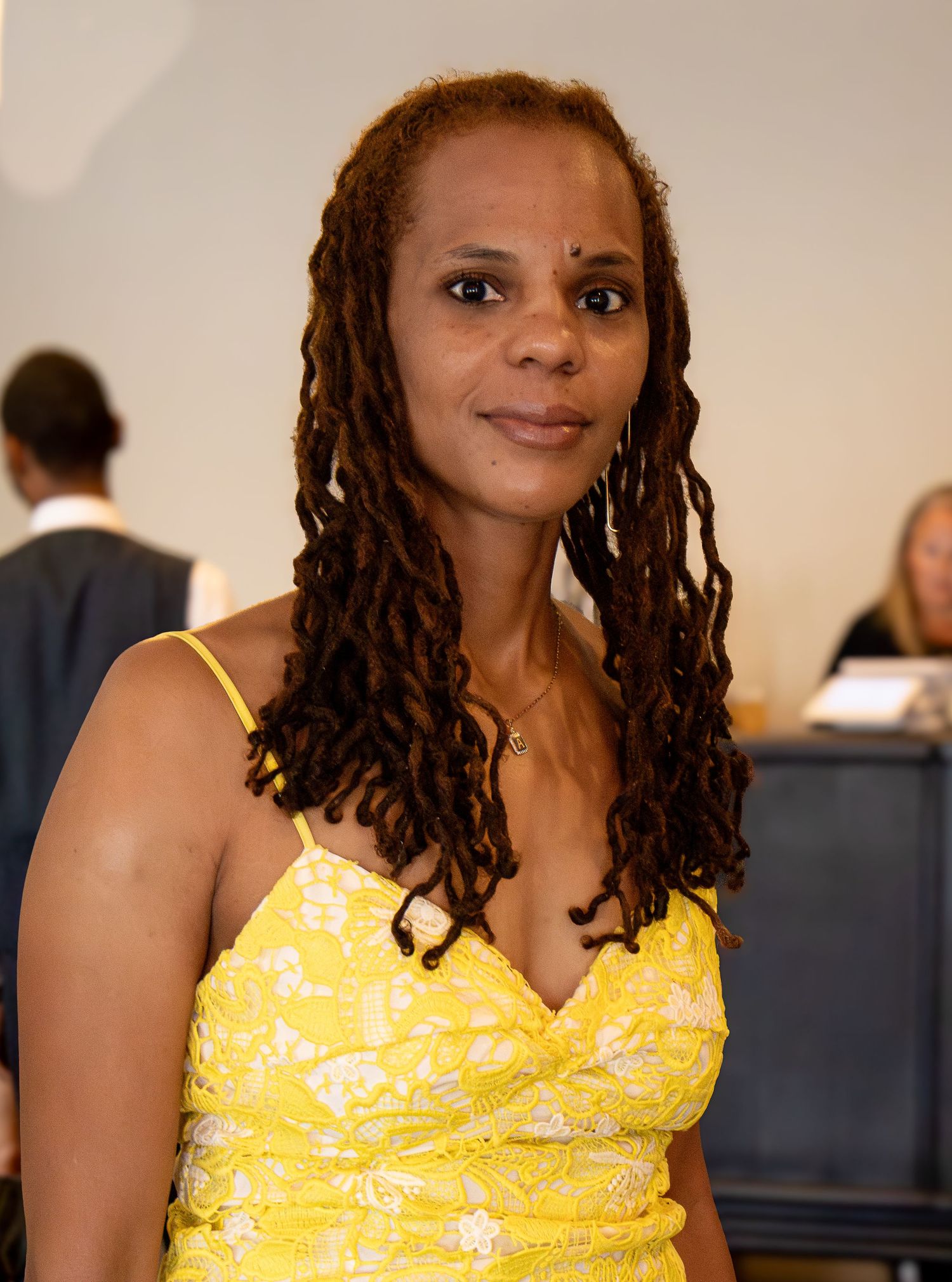Woman in bright yellow dress with locs hairstyle poses at formal event.