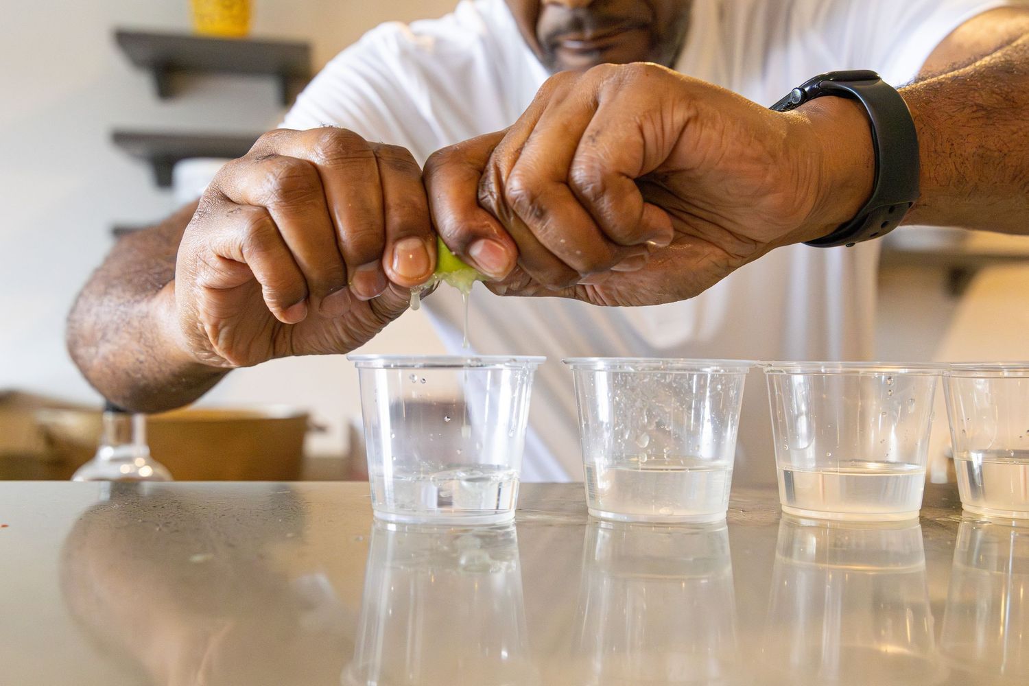 Hands cracking an egg over multiple clear shot glasses on a stainless steel counter.