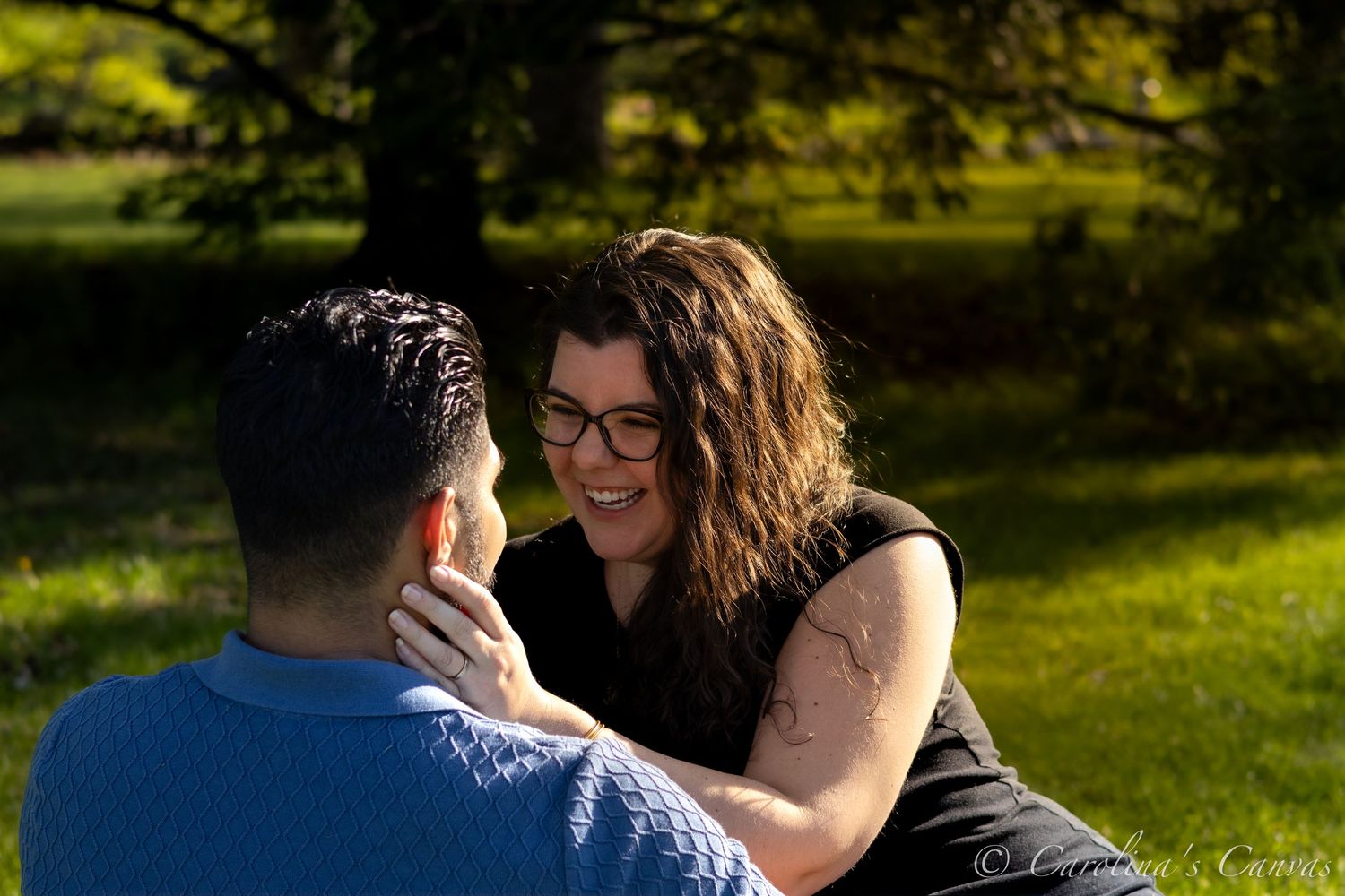 A couple sits together in a sunny park on a warm afternoon, sharing an intimate moment in the grass.