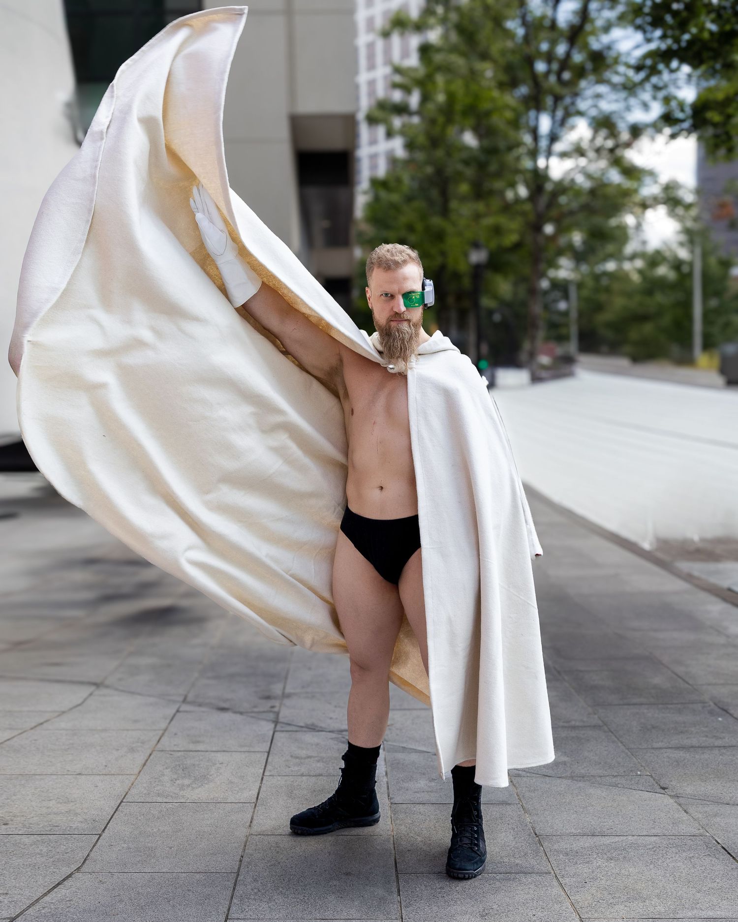 A figure in black boots performs a flowing movement with a billowing white fabric in an urban setting.