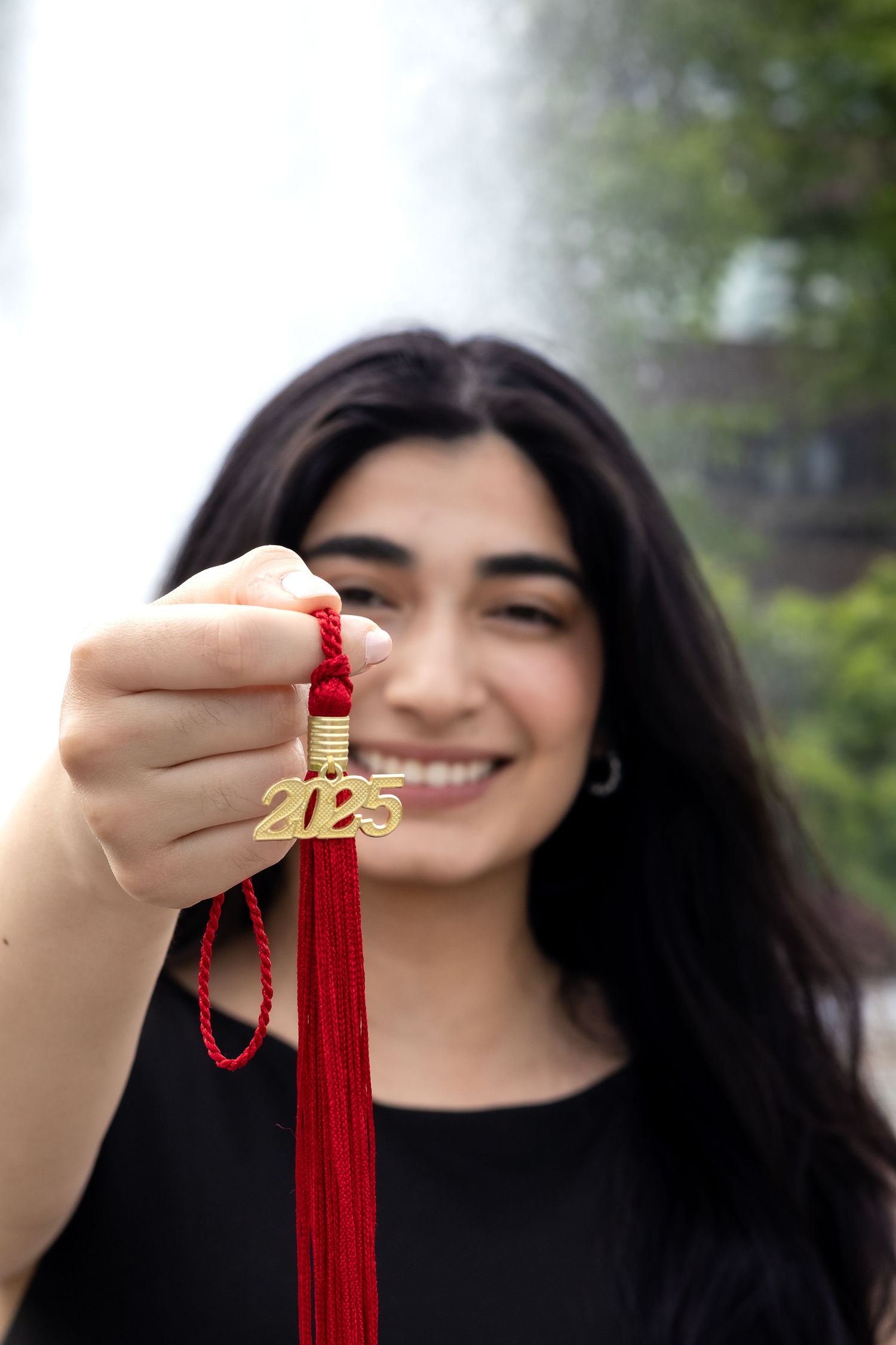 A graduate holding a red graduation tassel with gold 2023 charm against a blurred outdoor background.