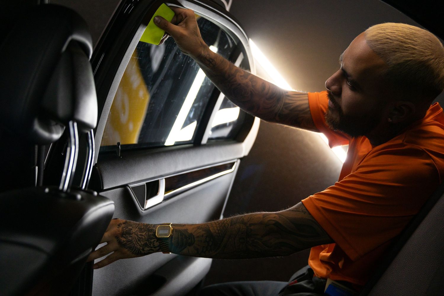 A person in an orange shirt inspects and details the interior of a dark vehicle with multiple camera angles shown. marketing and business ph