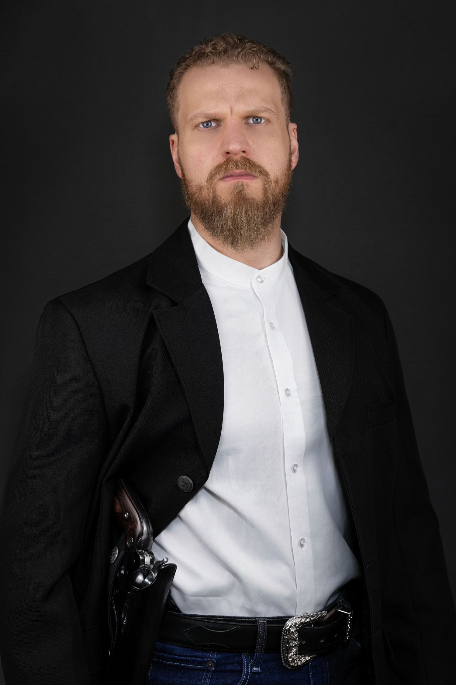 Professional studio portrait of someone wearing a black suit jacket and white dress shirt against dark background.