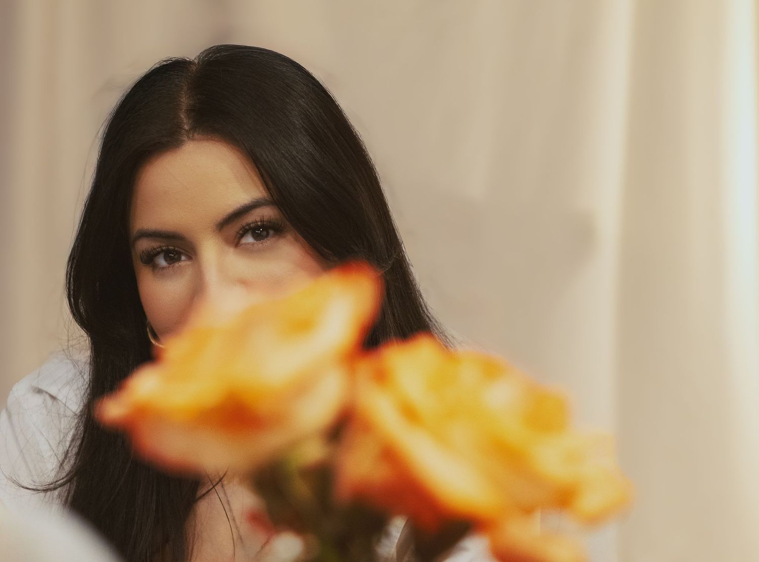 A person with dark hair is framed behind orange roses that blur into the foreground creating a dreamy portrait effect.