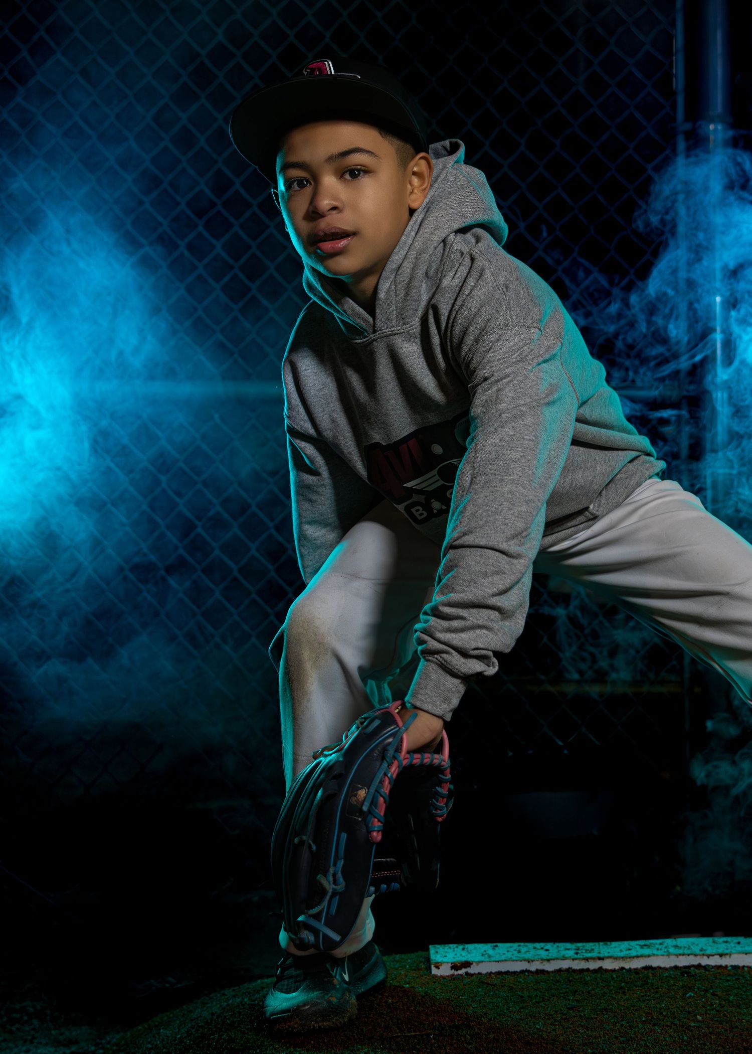 Athletic figure in gray hoodie crouching against blue smoke background.