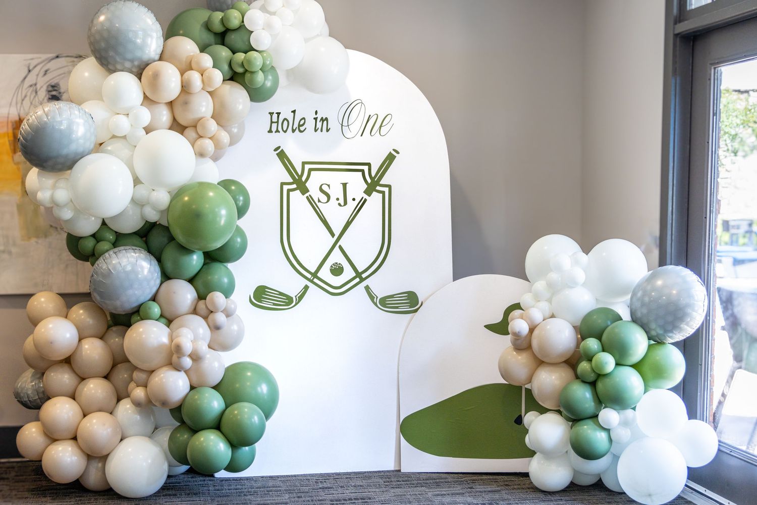 Elegant balloon arch installation in white, sage green, and gold colors creates a modern party decoration display.