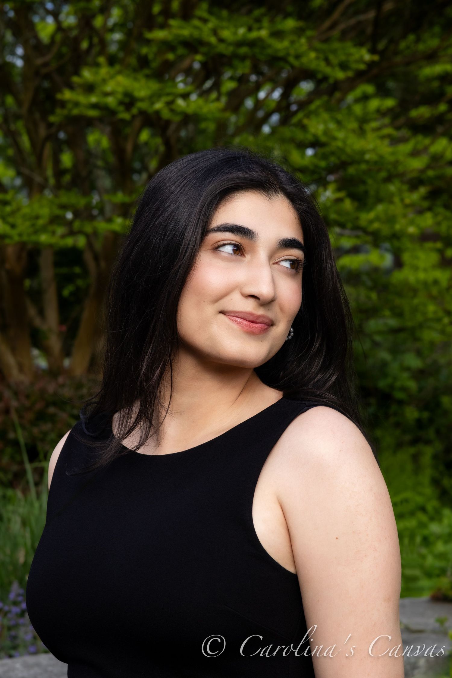 Portrait photograph in an outdoor garden setting with lush green foliage in the background.