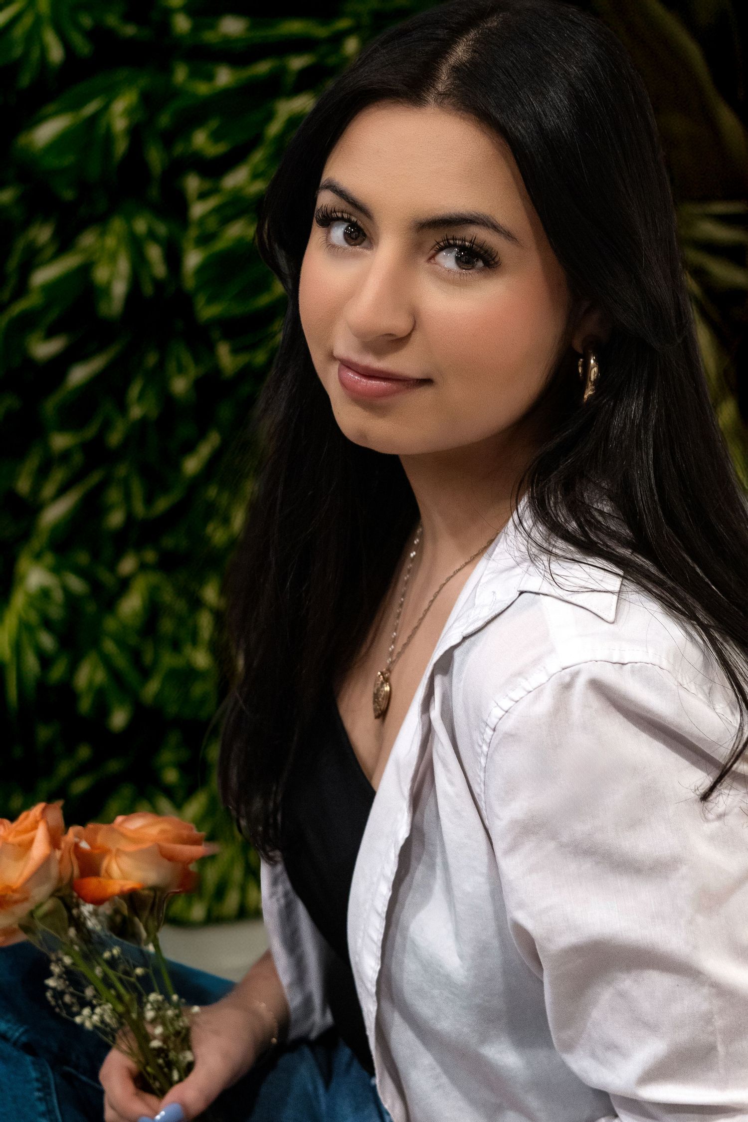 Young woman in a white button-down shirt poses with orange flowers against a green garden backdrop.