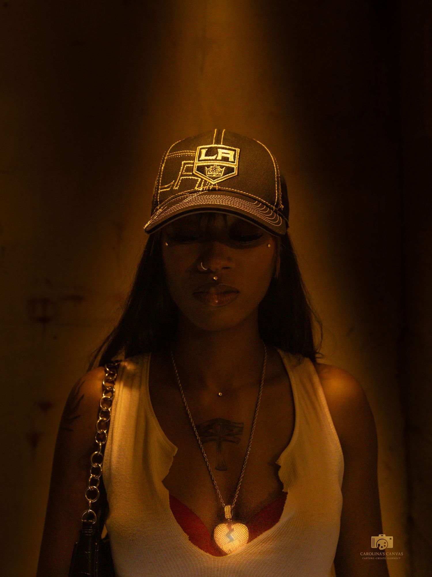 Young woman in LA Kings cap and gold chain necklace poses under warm golden light in urban setting.