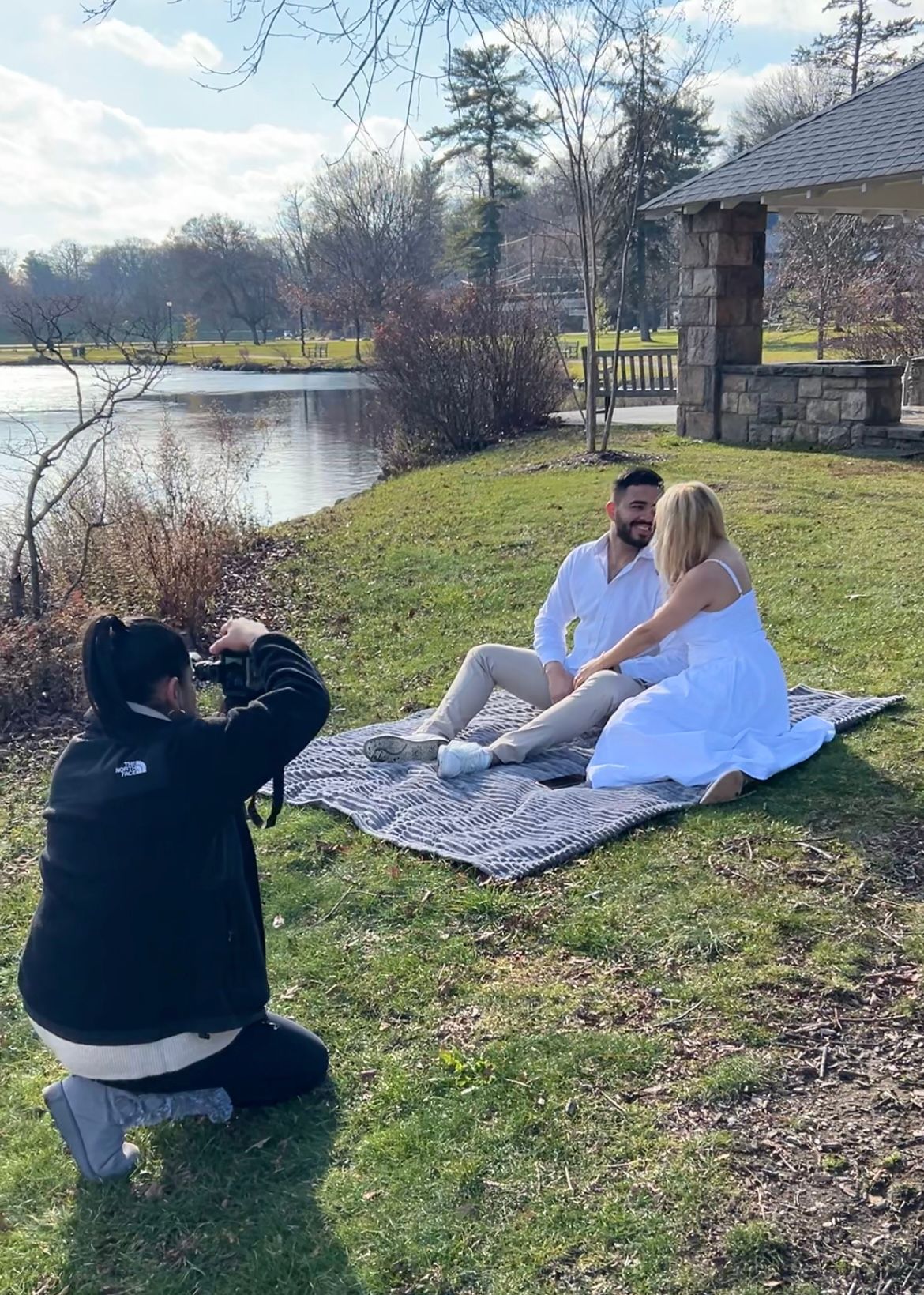 People enjoying a relaxing afternoon on a grassy hill overlooking a serene lake on a cloudy day. local photographer