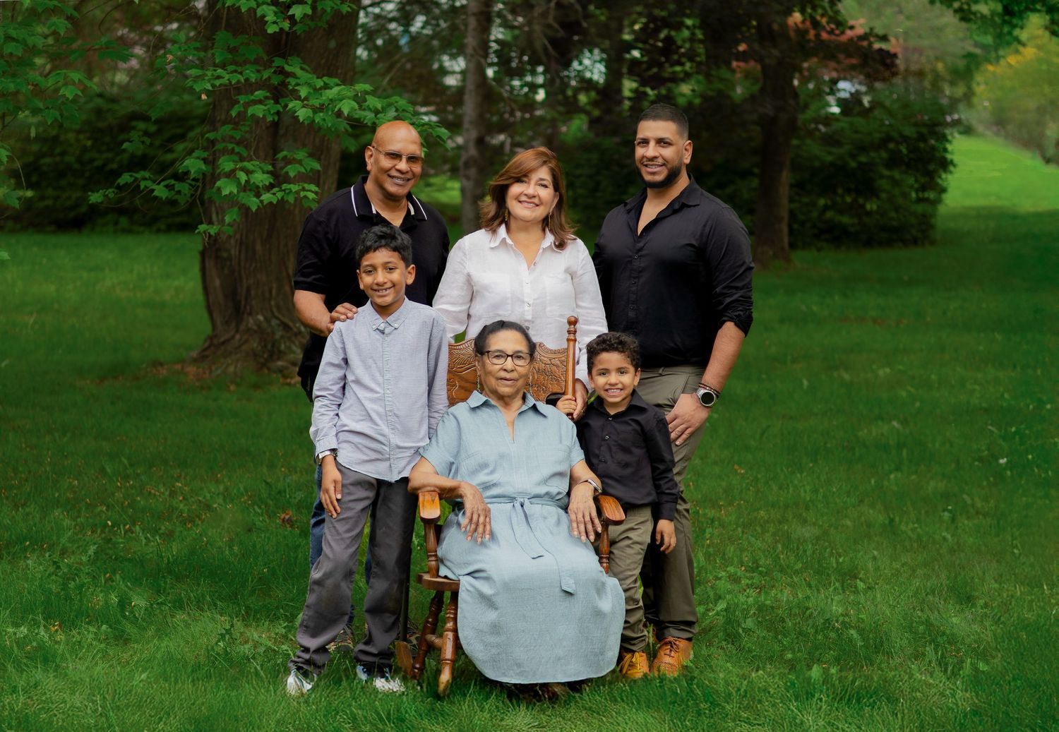 A group of six people pose together on a grassy lawn with trees in the background.