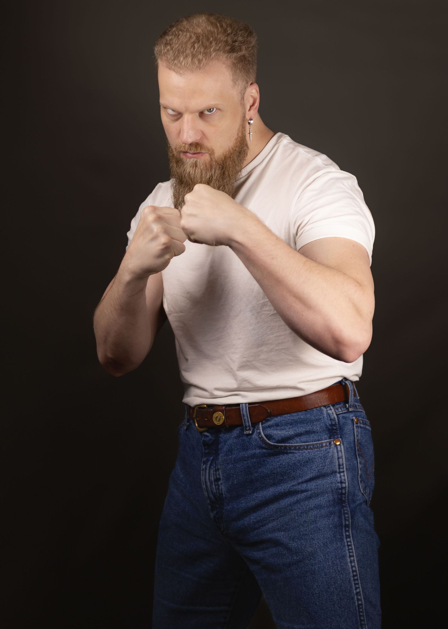 Boxer in white t-shirt and jeans demonstrates self-defense combat stance against dark background.