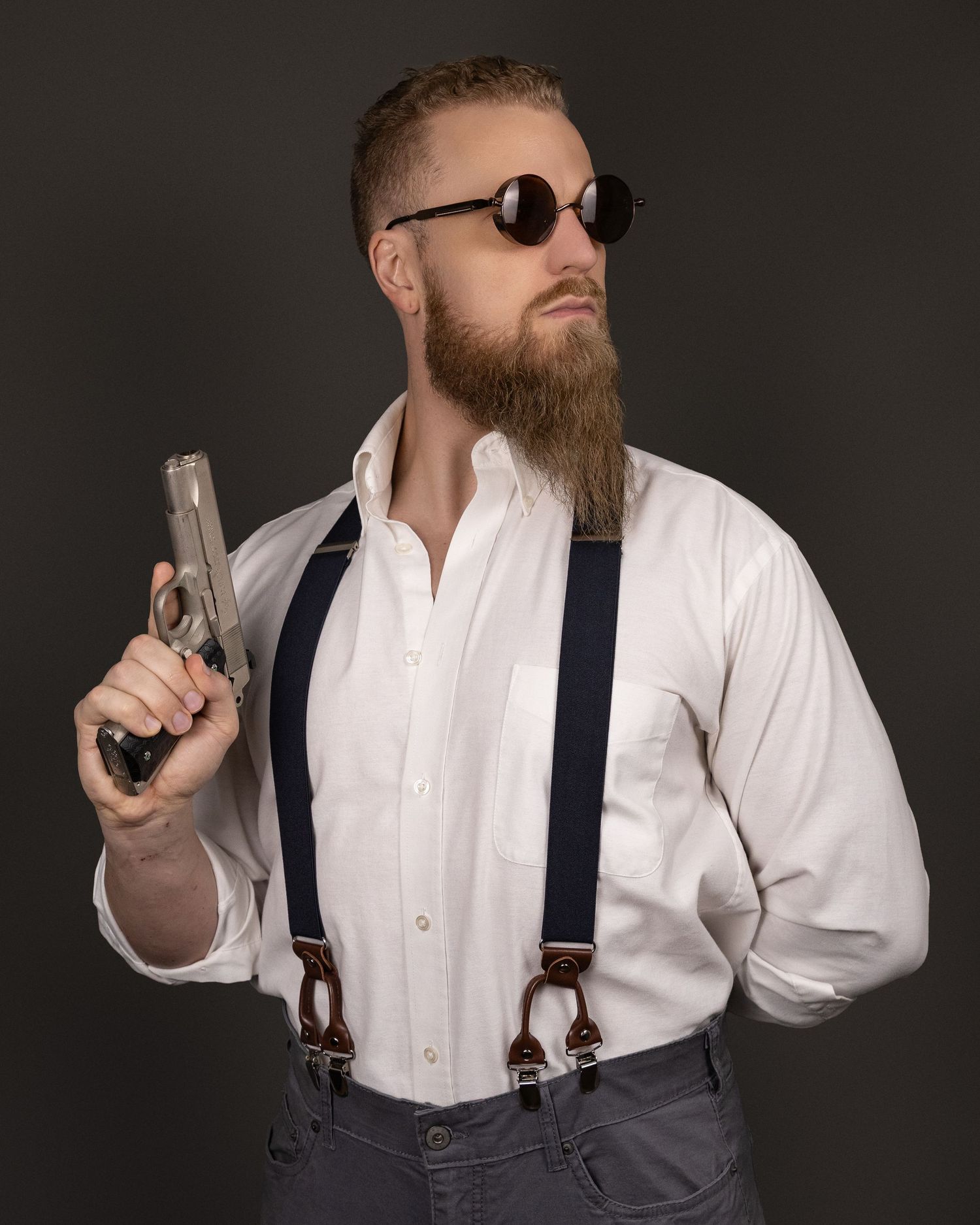 A bearded man in a white dress shirt and suspenders poses with a handgun in a series of dramatic studio shots.