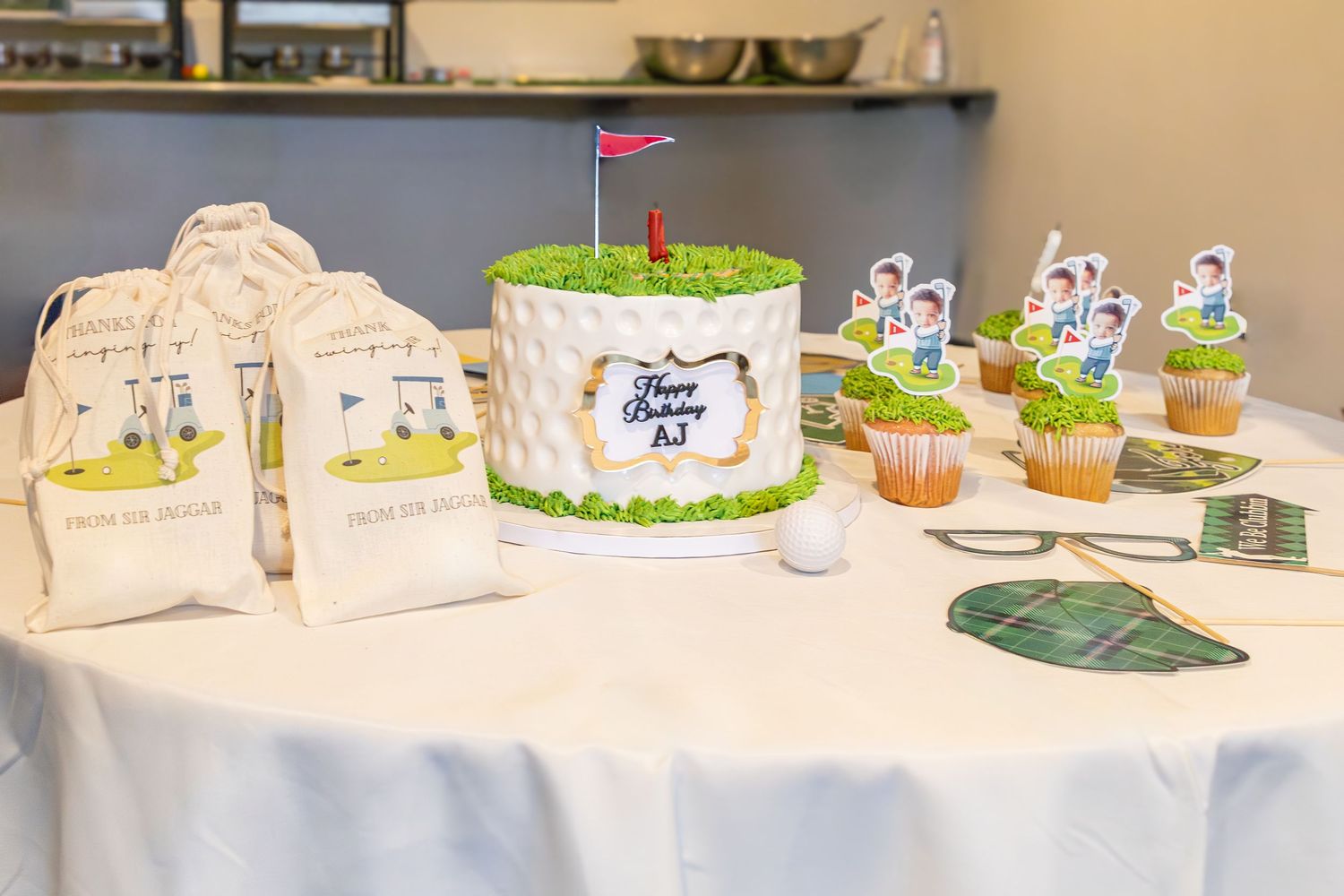A wedding dessert table with a white cake, cupcakes, and decorative place cards on an elegant white tablecloth.