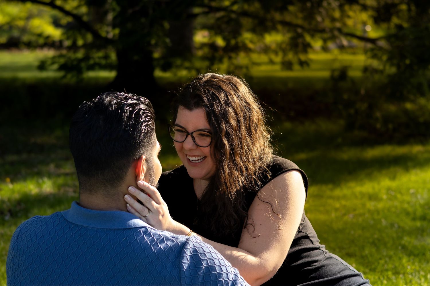 A couple shares an intimate moment together while sitting outdoors in a sunny park setting.