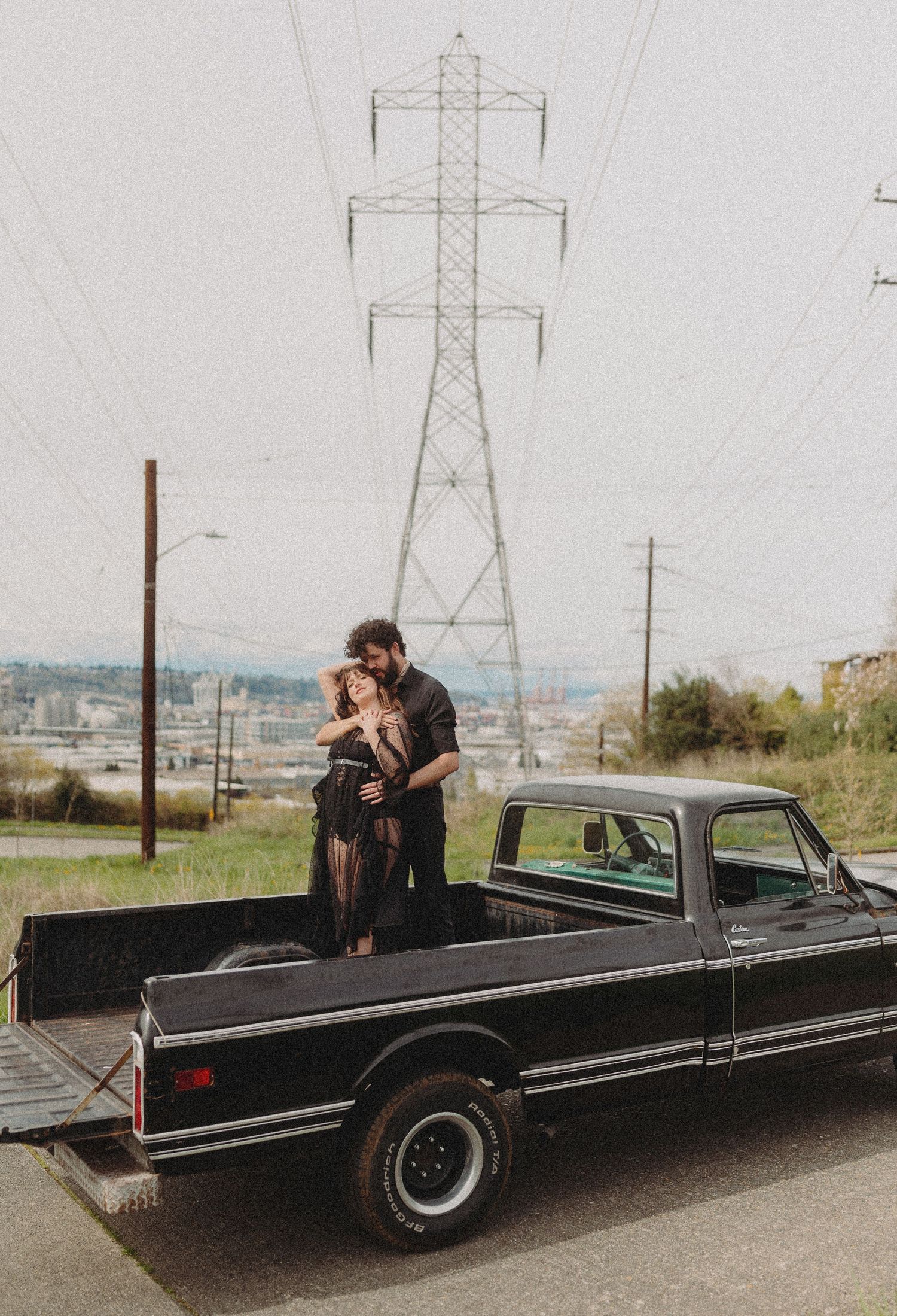 A couple standing in the bed of a pickup truck with a power transmission tower in the background.