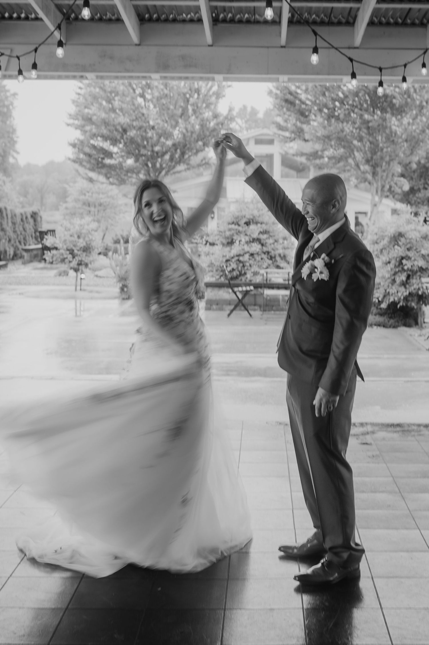 A couple dancing on a covered patio with string lights overhead, captured in black and white.