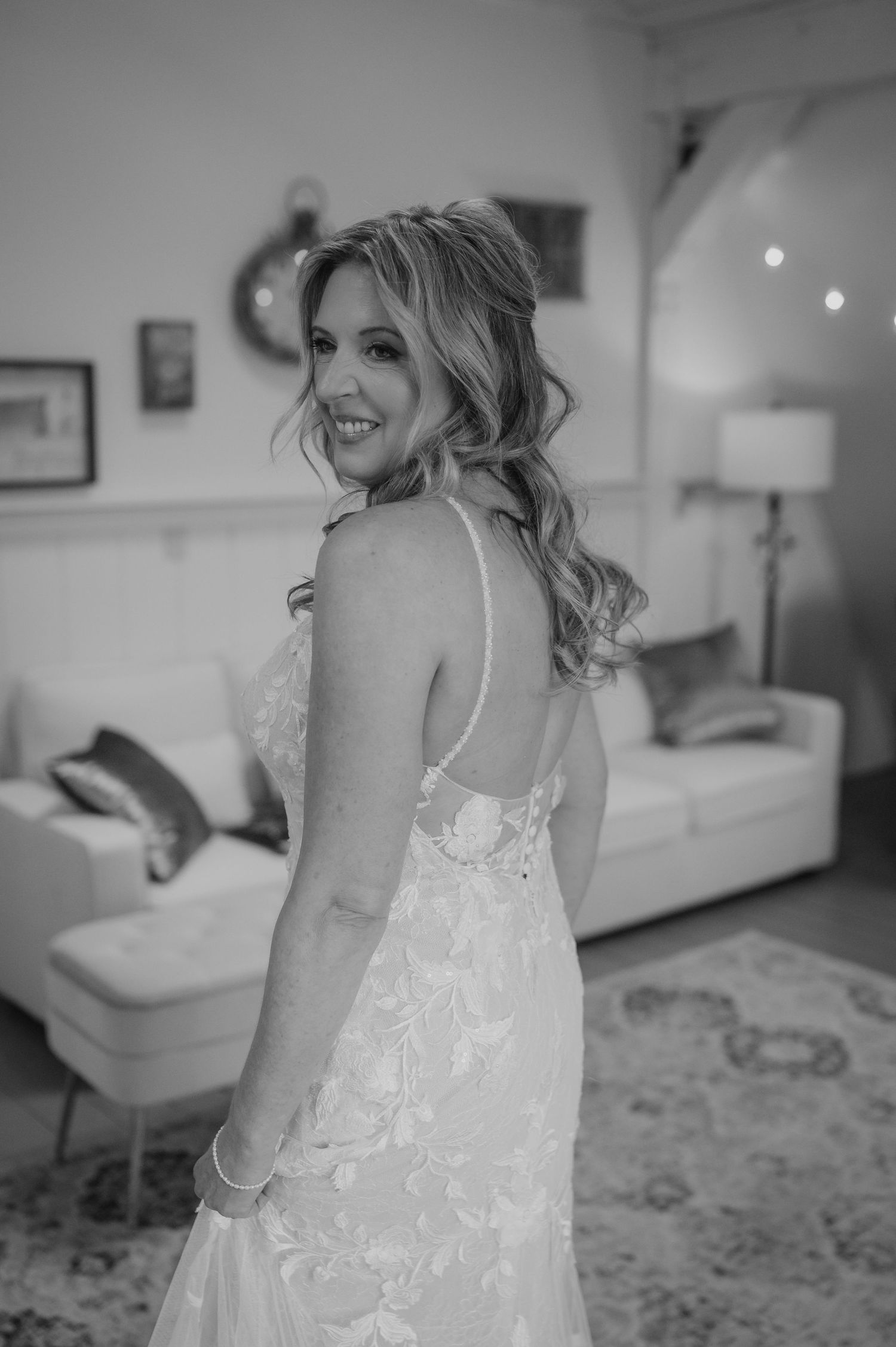 Black and white portrait of a bride in a lace dress smiling in an indoor setting.