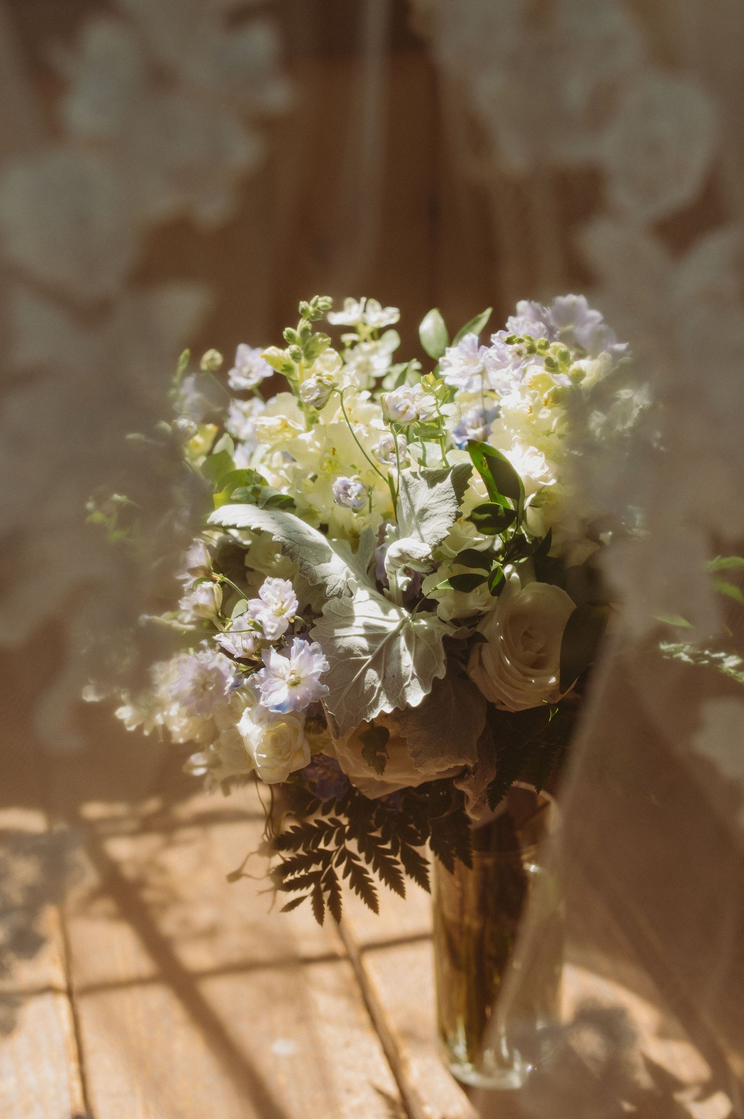 A delicate floral arrangement of white and pale pink blooms with ferns in a glass vase casting soft shadows.