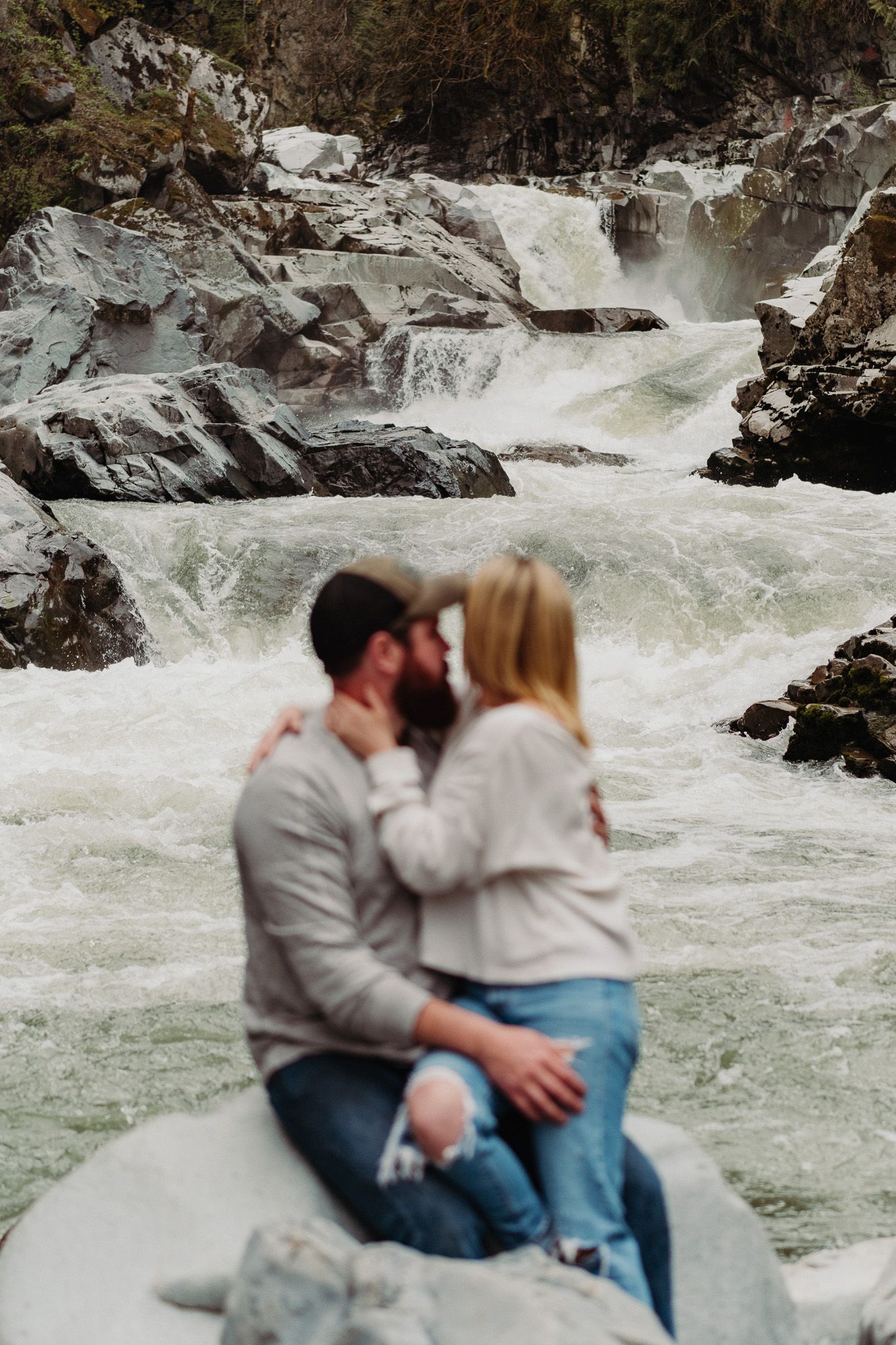 Couple sharing an intimate moment on a rock overlooking rushing white water rapids.
