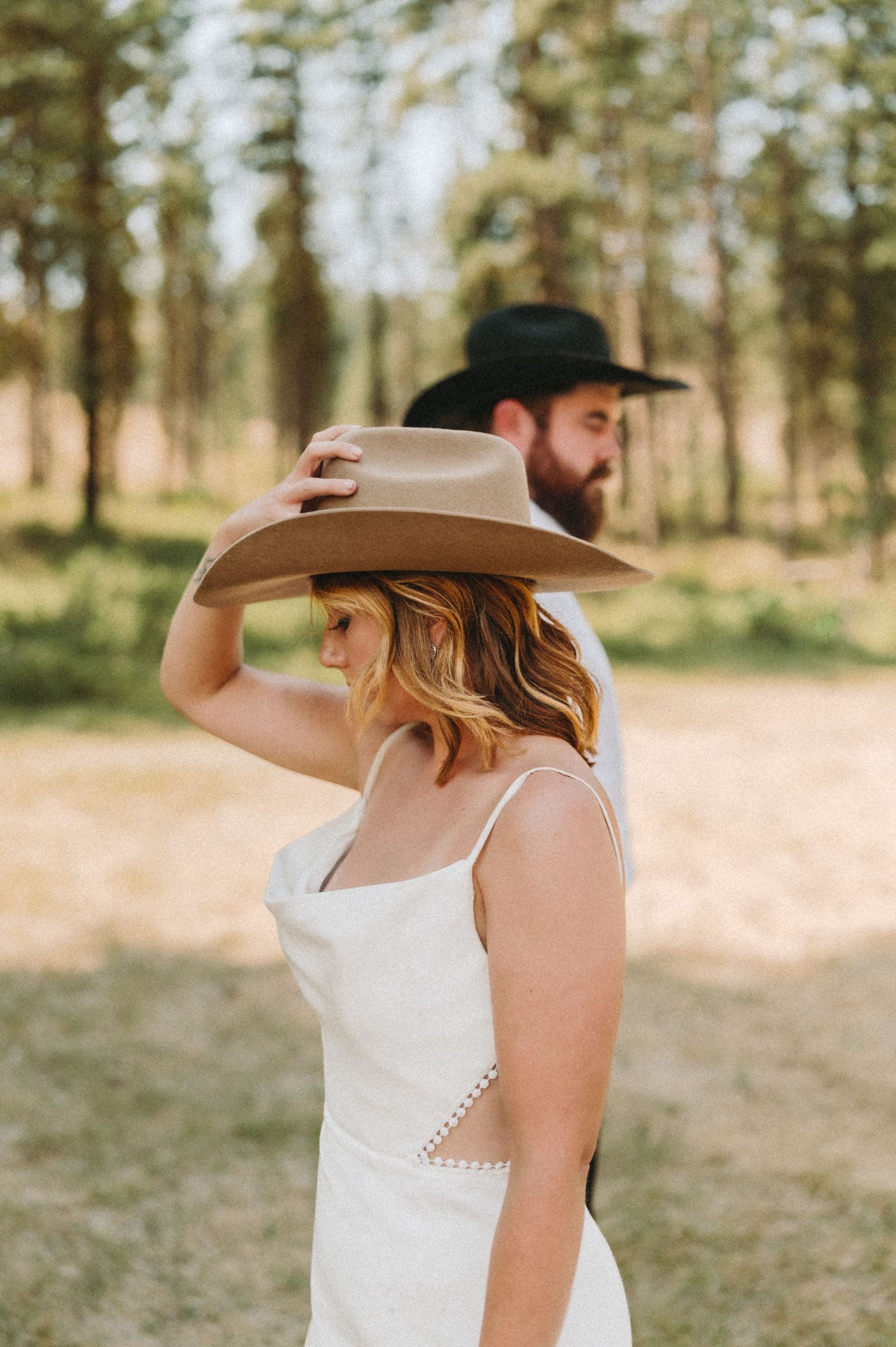Two people in western hats standing in a sun-dappled forest clearing.