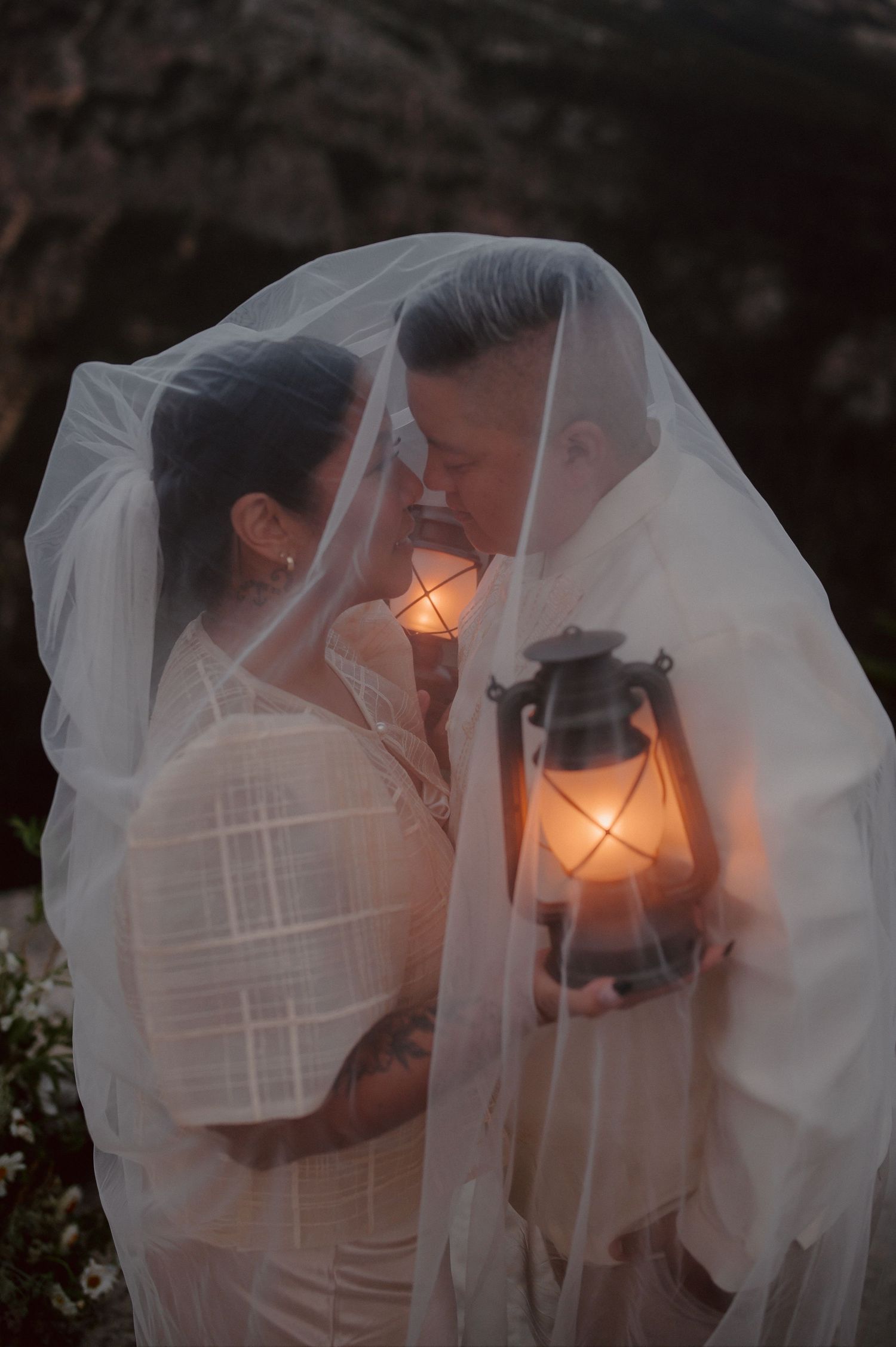 A romantic wedding couple shares an intimate kiss under a flowing white veil at sunset.