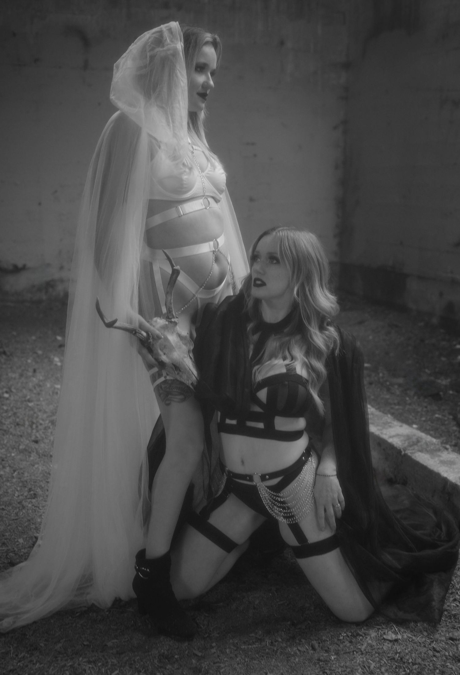 Artistic black and white image showing two people in bondage-inspired outfits with contrasting white veil and dark clothing.